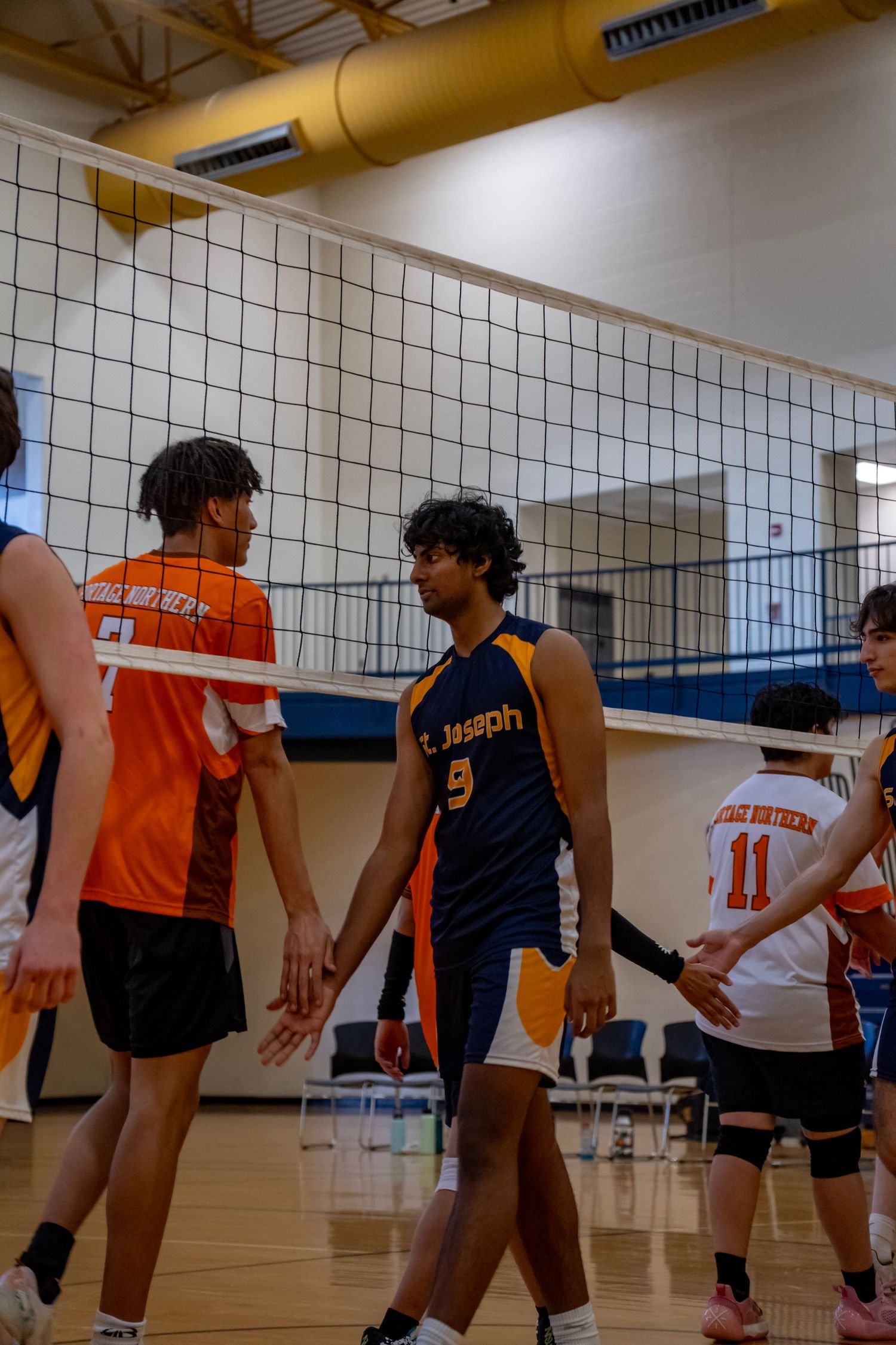 Players in orange and navy uniforms interact during a volleyball match.