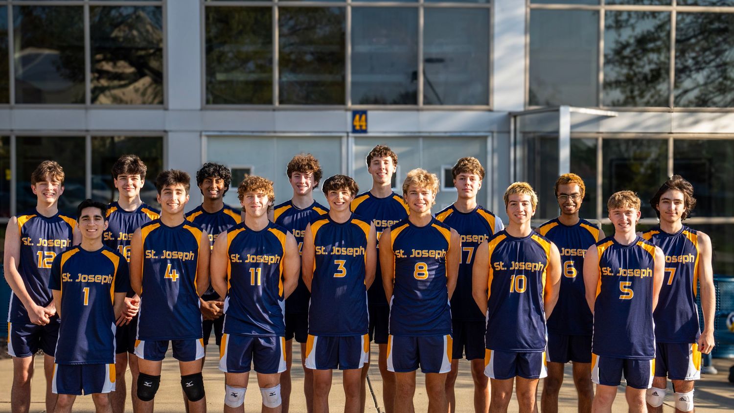 High school volleyball team standing in formation wearing navy blue uniforms for team photo.