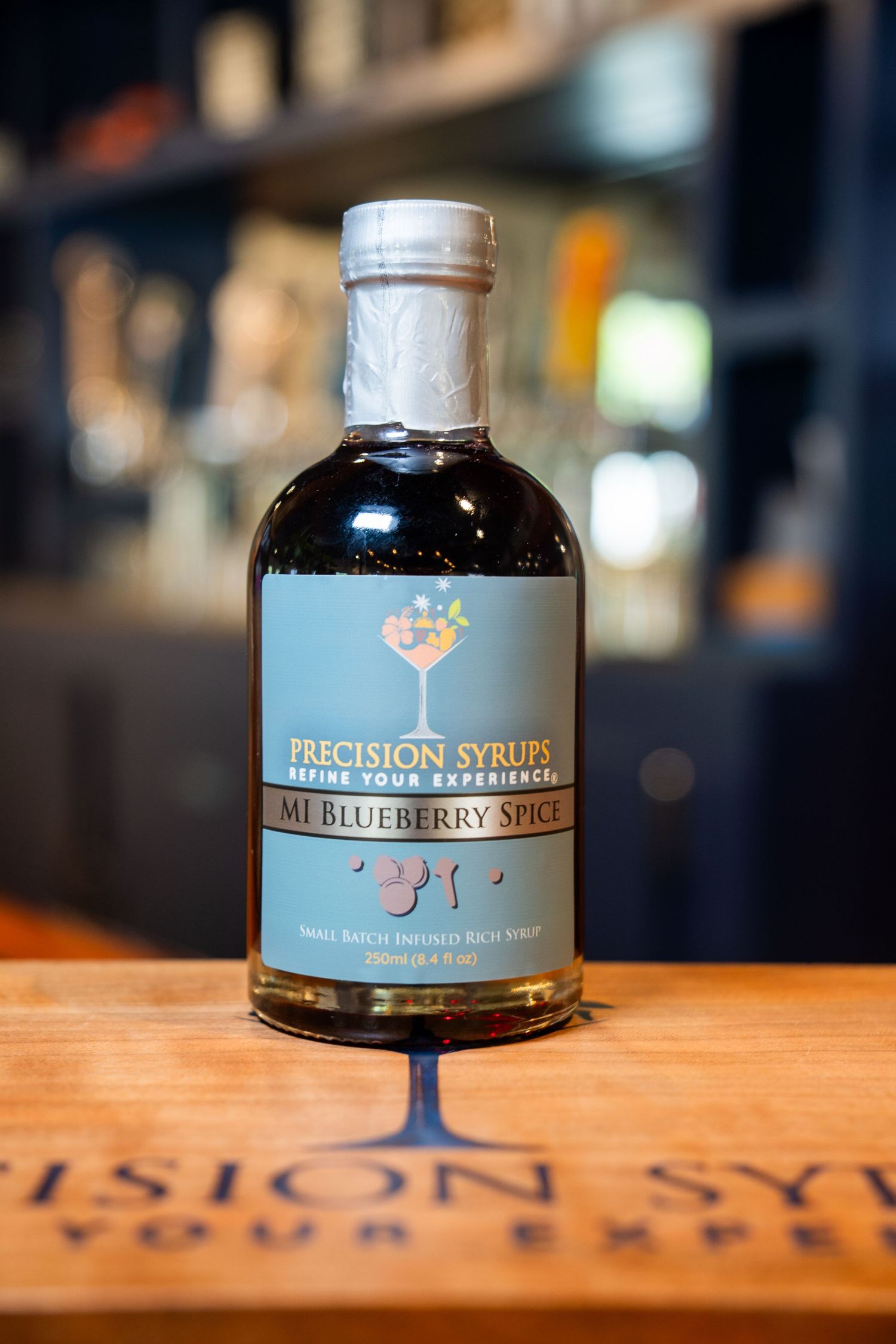 Bottle of Precision Syrups blueberry mule mixer on wooden surface.