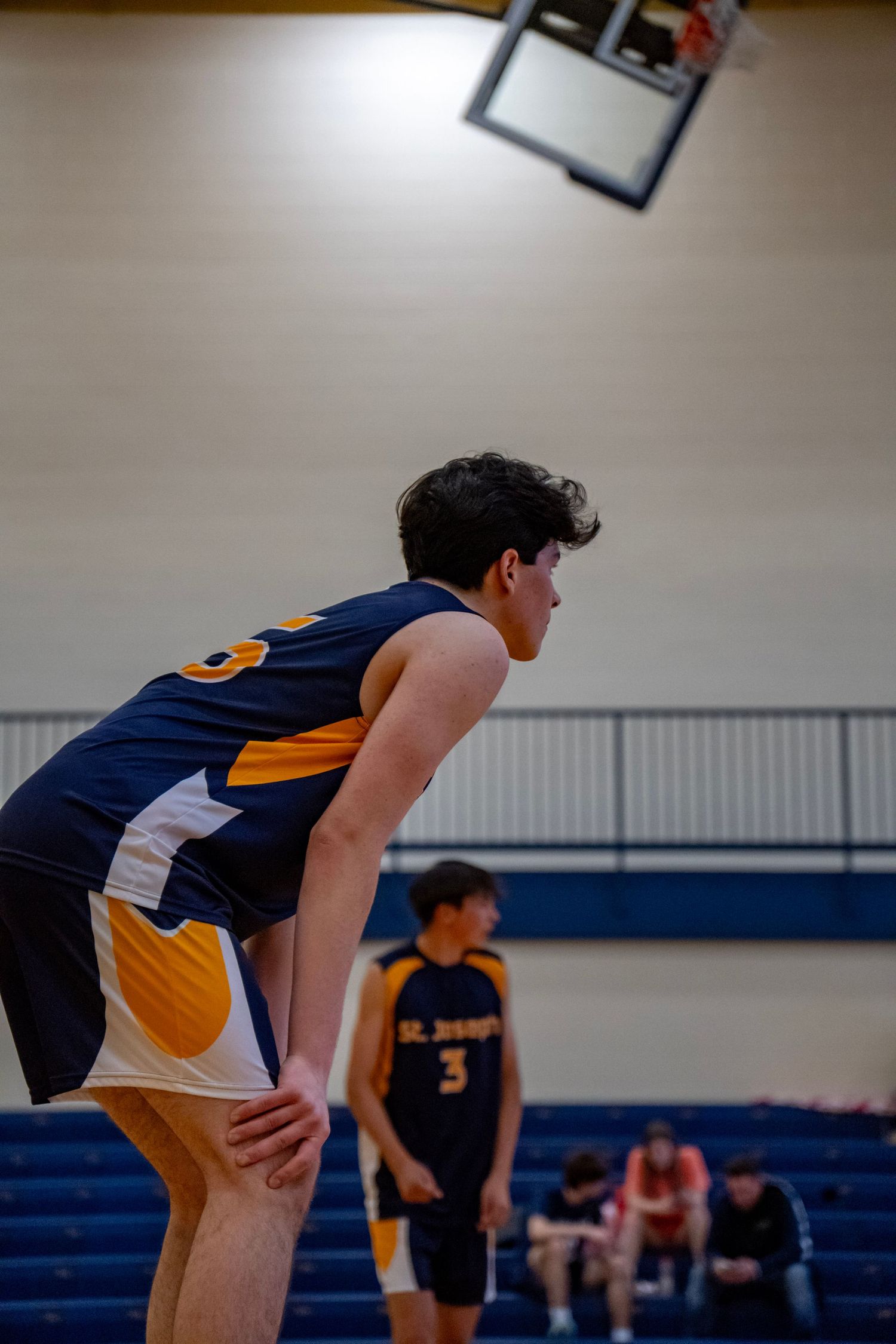 Basketball player in navy and gold uniform bent over catching their breath during game break.