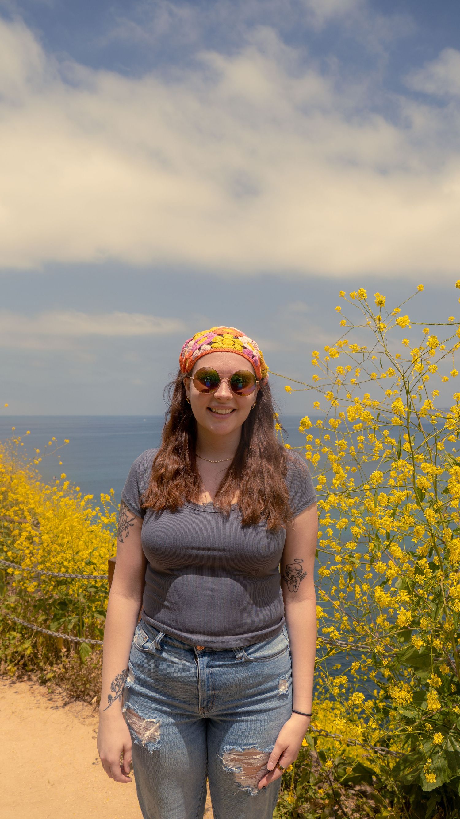 Casual summer outfit with bandana and sunglasses against backdrop of coastal flowers and ocean view.