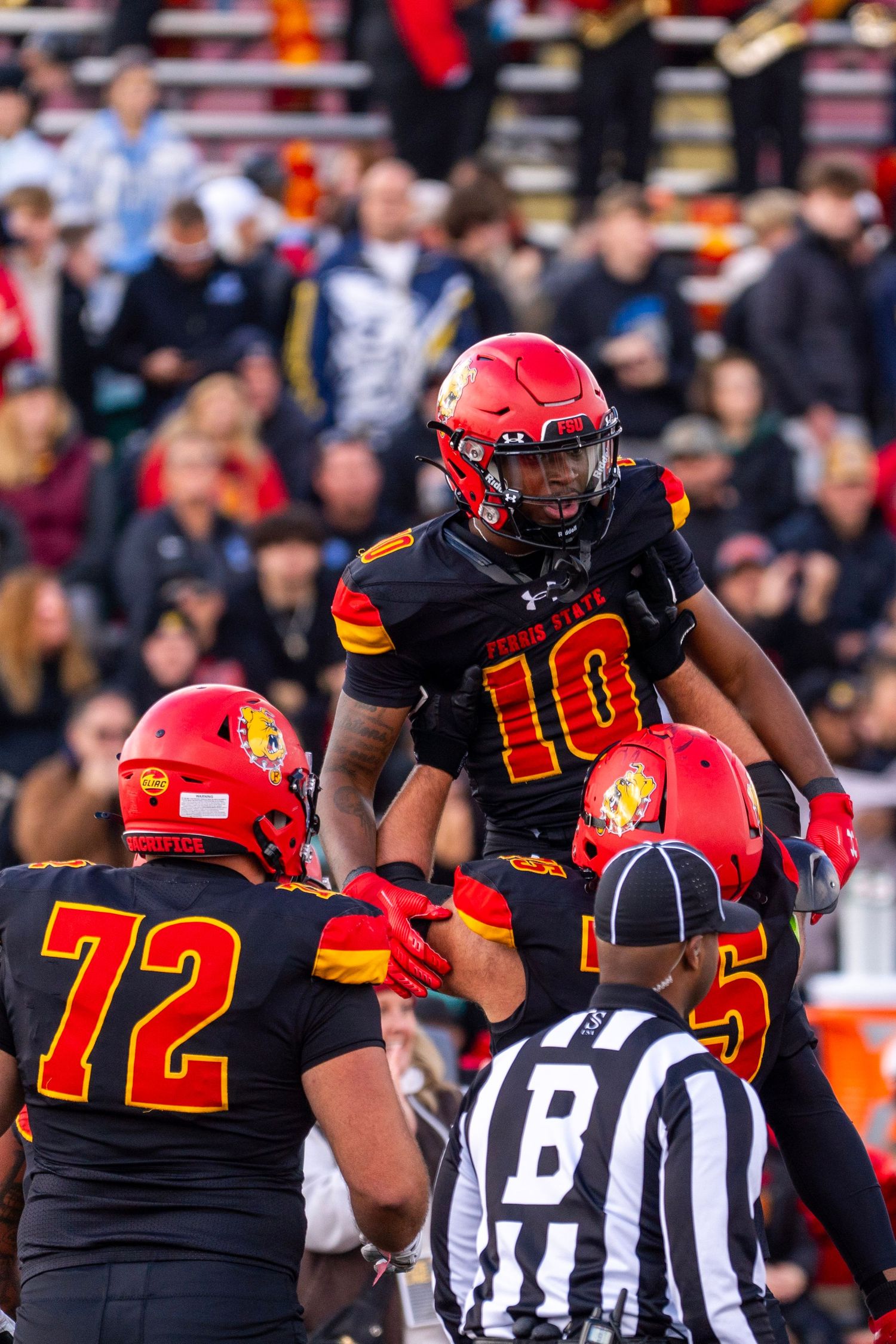 Football players in red helmets and black jerseys huddle with officials in striped uniforms during a game.