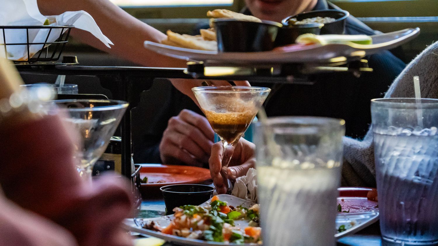 Diners seated at a long restaurant table featuring shared plates and casual dining atmosphere.