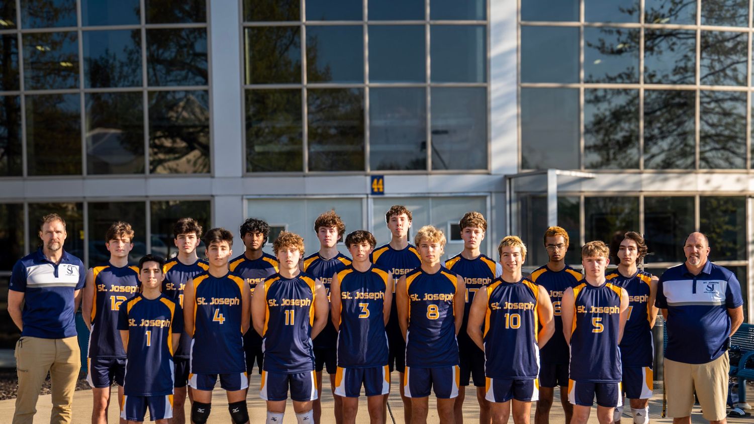 Youth basketball team in navy uniforms posed for group photo in front of glass building.