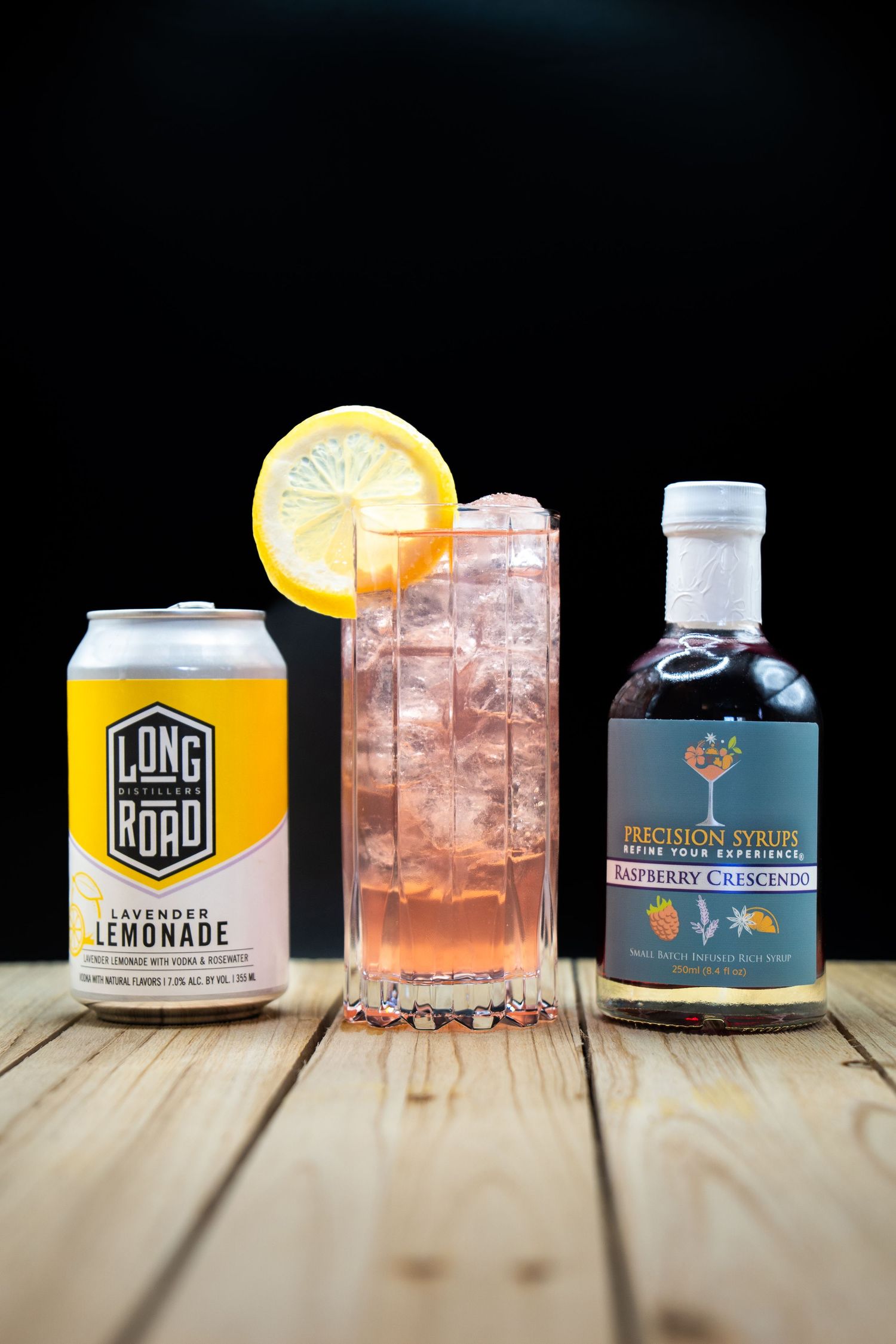 Long Road lemonade can beside pink cocktail and craft spirits bottle on wooden table.