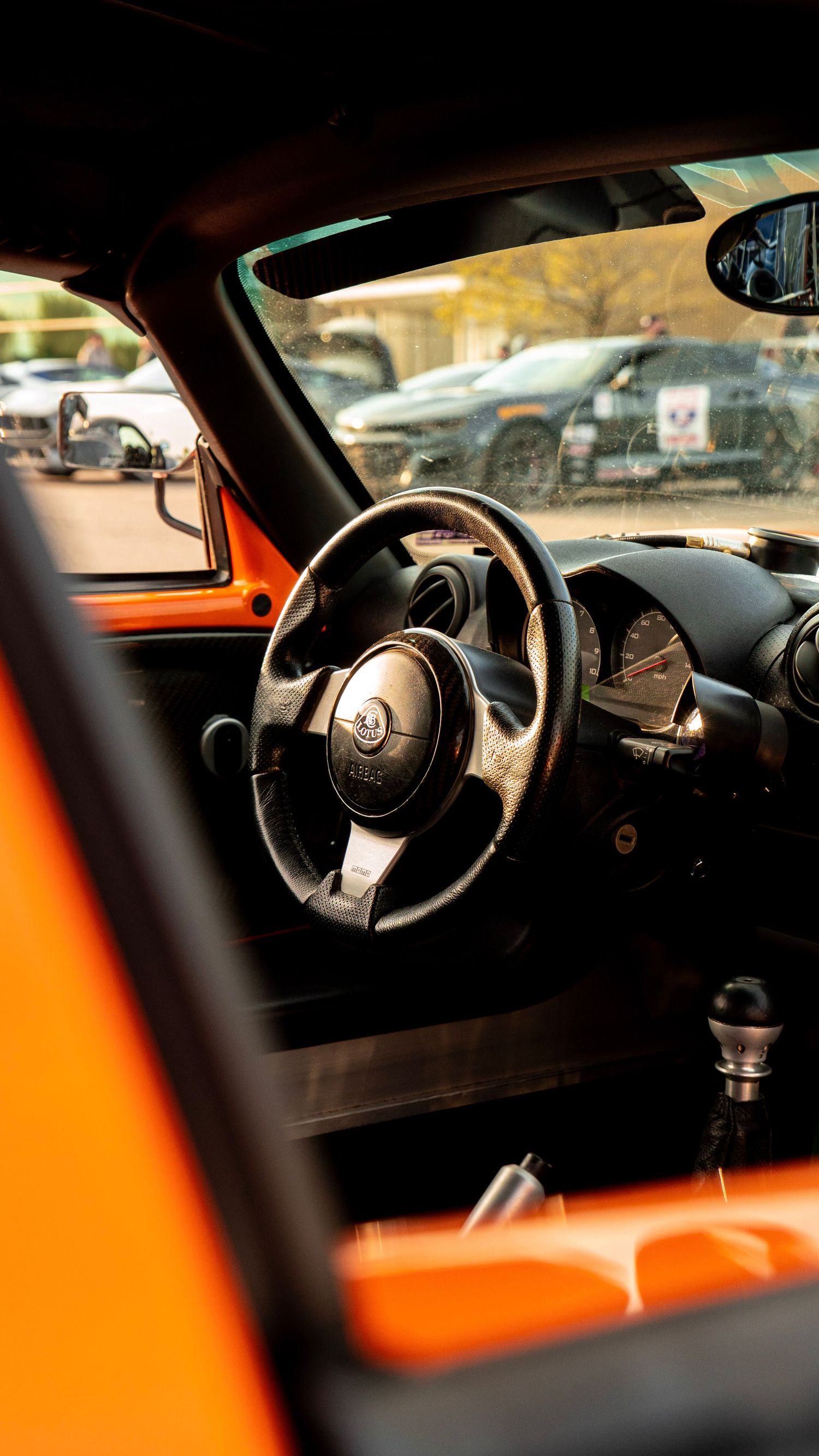 Interior dashboard view of orange Lotus vehicle with leather steering wheel.