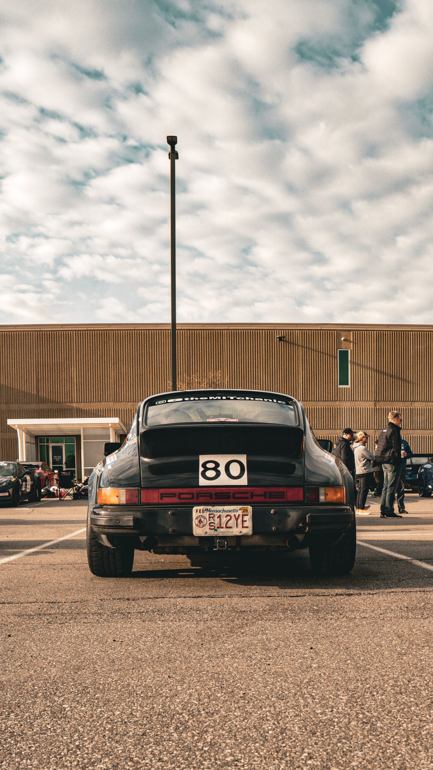 Black Porsche 911 race car with number 80 photographed from behind in a parking lot setting.