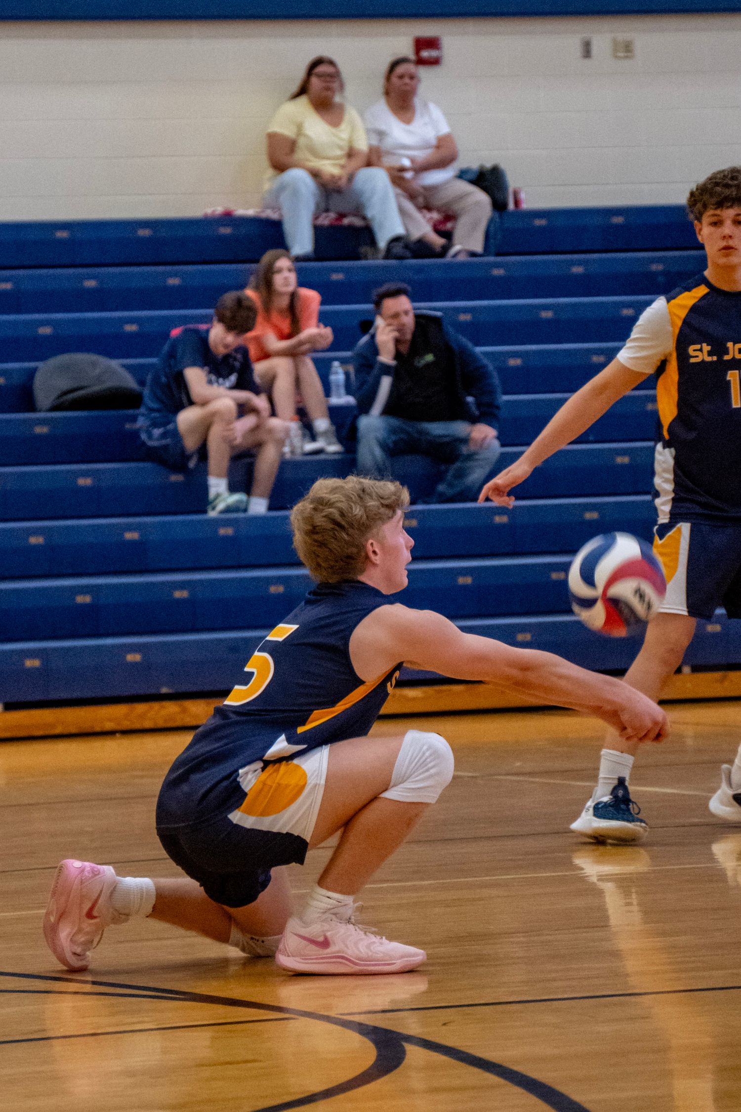 Player dives across the hardwood floor to save a volleyball during an intense game.