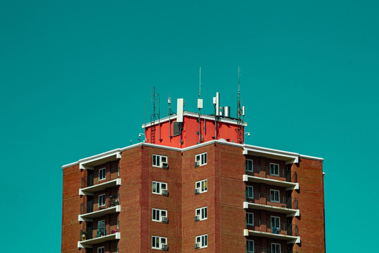 Modern brick apartment building with balconies against turquoise sky.