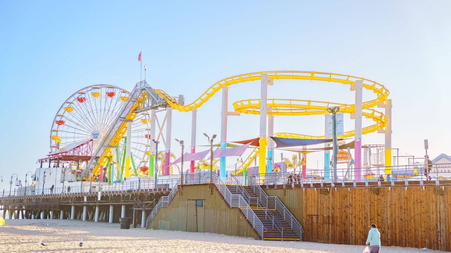Yellow roller coaster track and Ferris wheel at Pacific Park amusement pier.