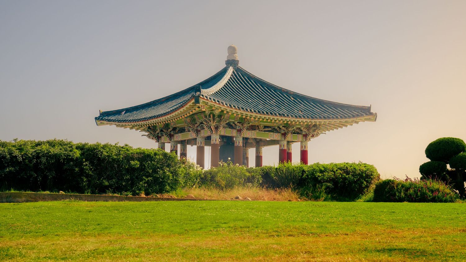 Korean style gazebo with ornate green roof surrounded by manicured gardens.