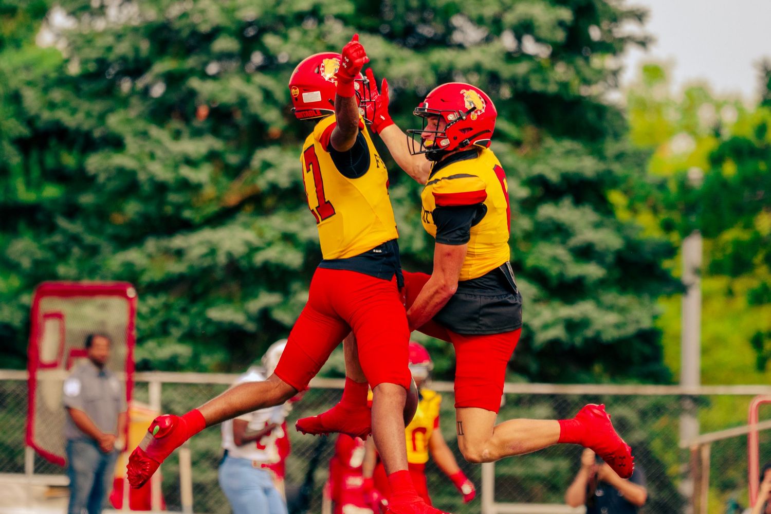 Football players in red and yellow uniforms practice blocking and tackling drills during training camp.