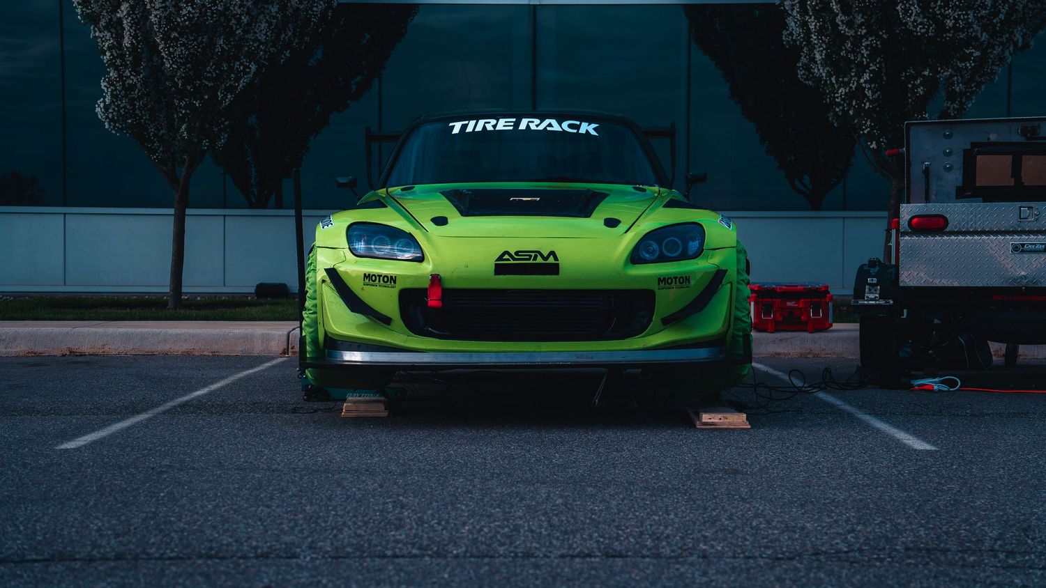 Front view of lime green Lotus race car in parking lot at dusk.