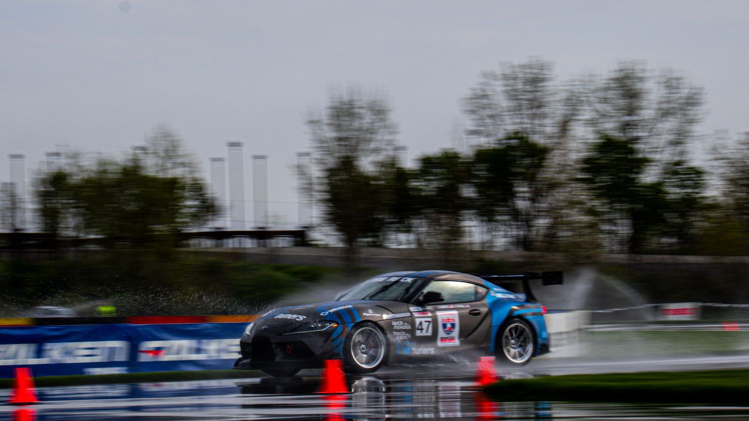 Race car drifting through wet track corner with spray flying.