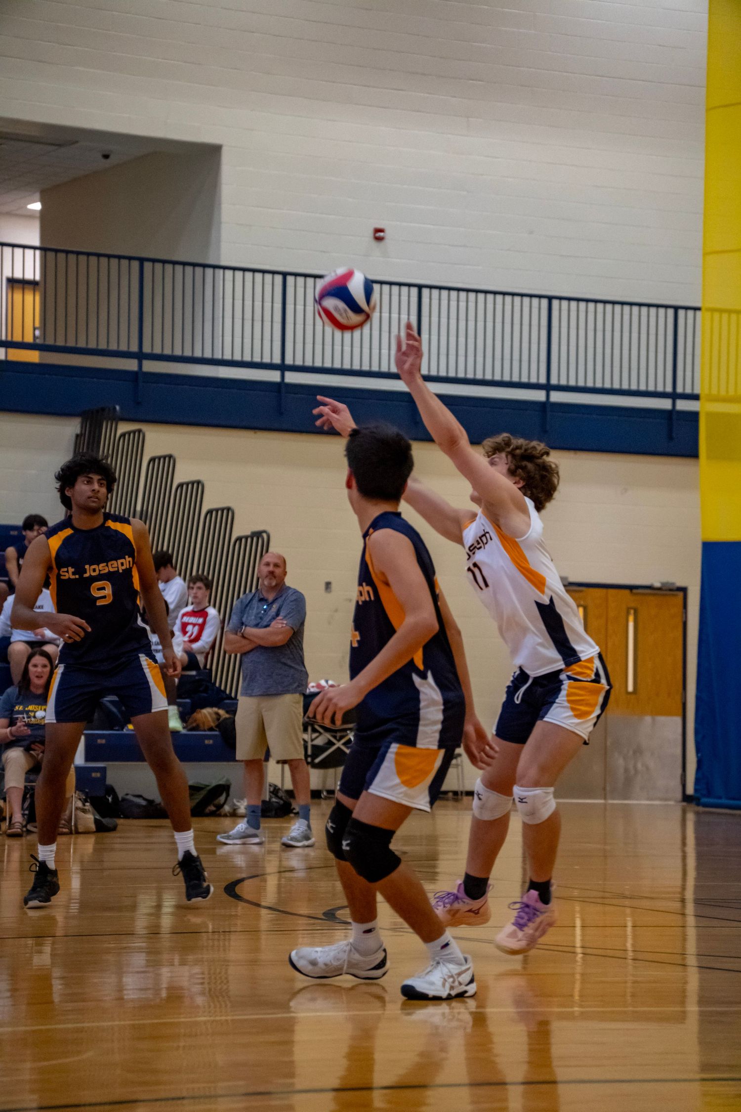Players battle for control during an intense volleyball point in a school gym.