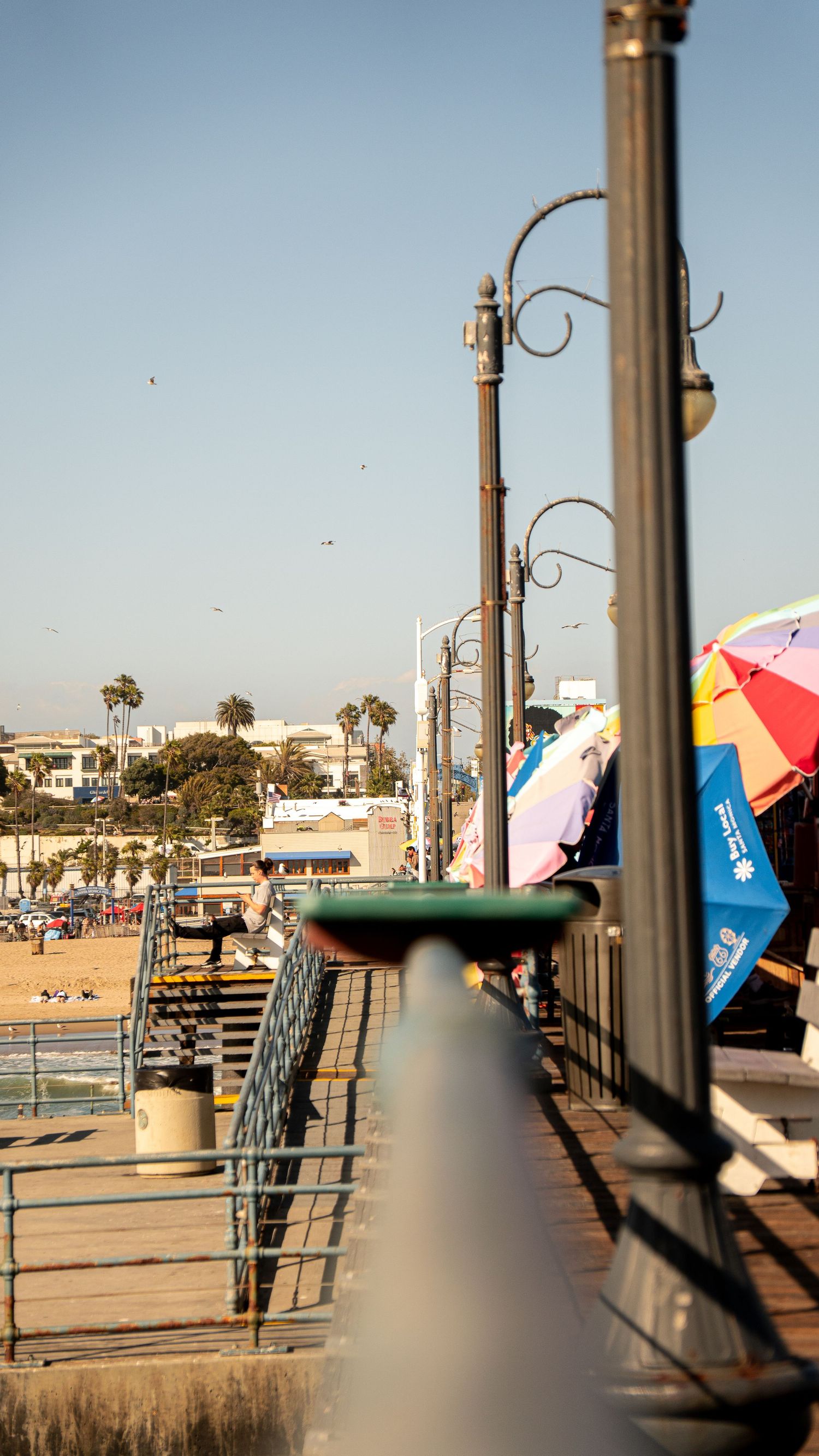 Vintage lampposts line the Santa Monica Pier boardwalk with beach and umbrellas in background.