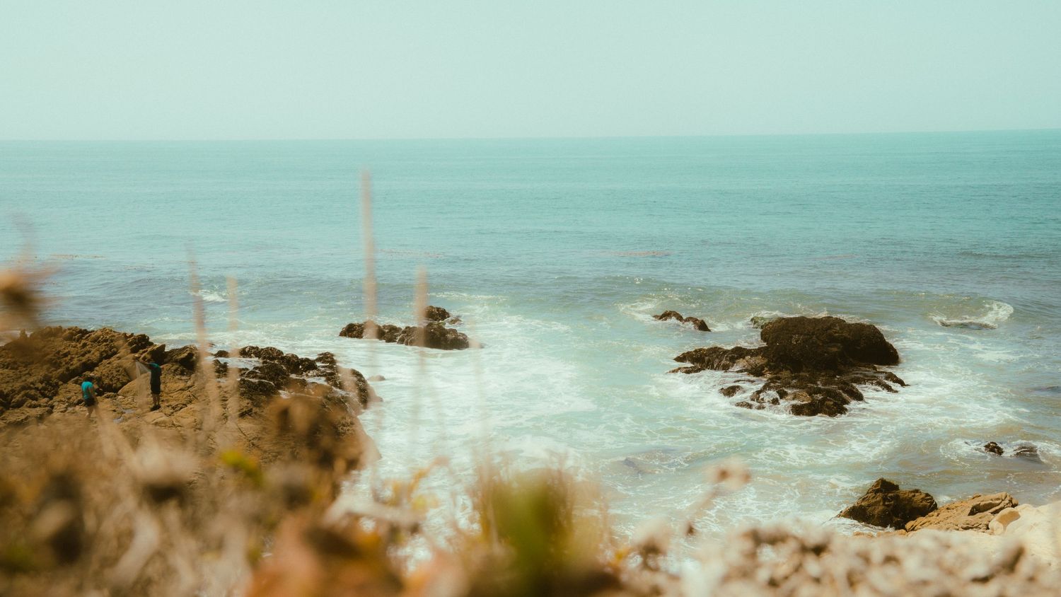 Panoramic view of a coastal beach with rocky formations jutting out into blue waters.