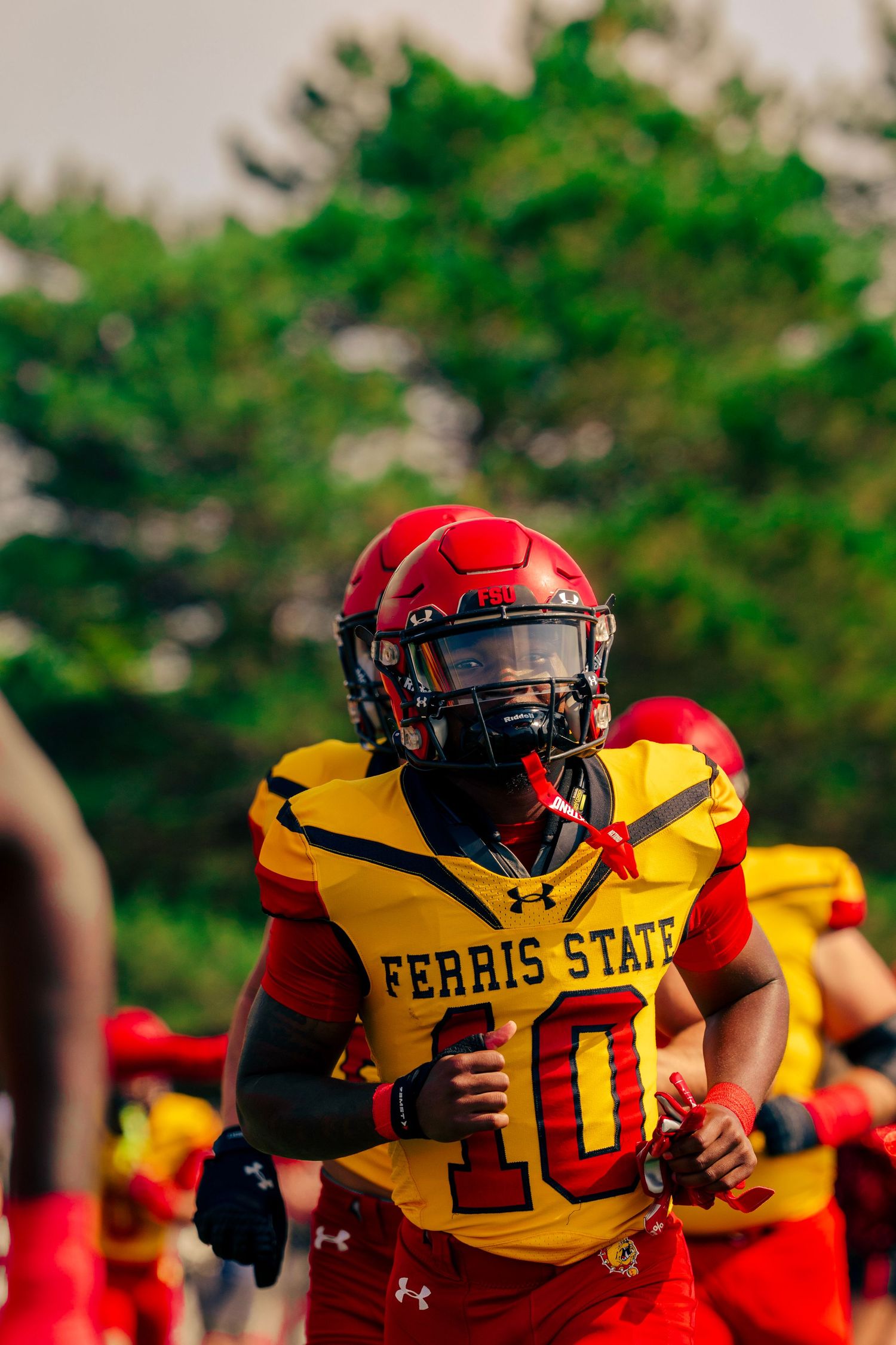 Football players in red and yellow Ferris State uniforms line up during a game on a sunny day.