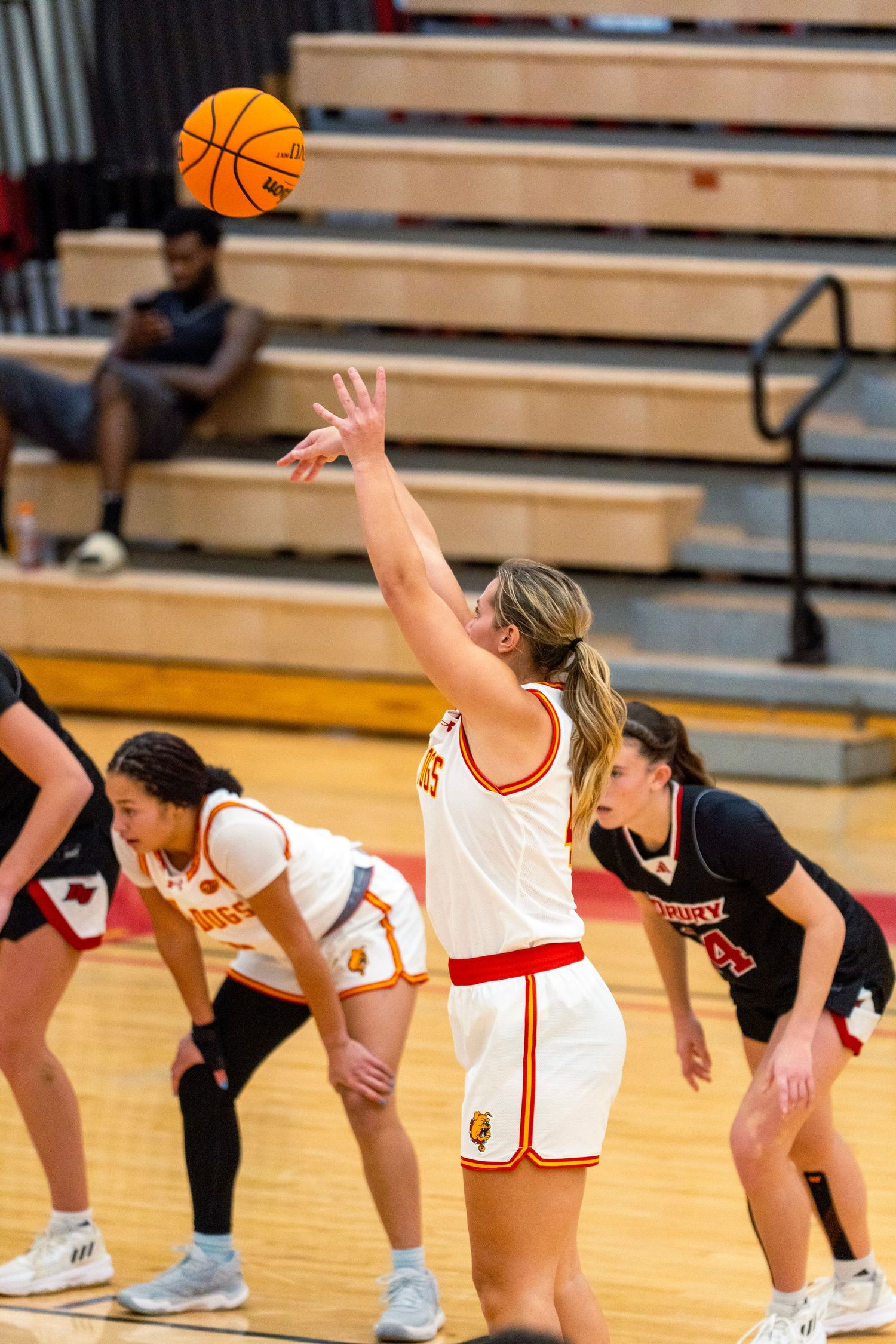 Multiple basketball players bend down in a line formation during a game on a gymnasium court.