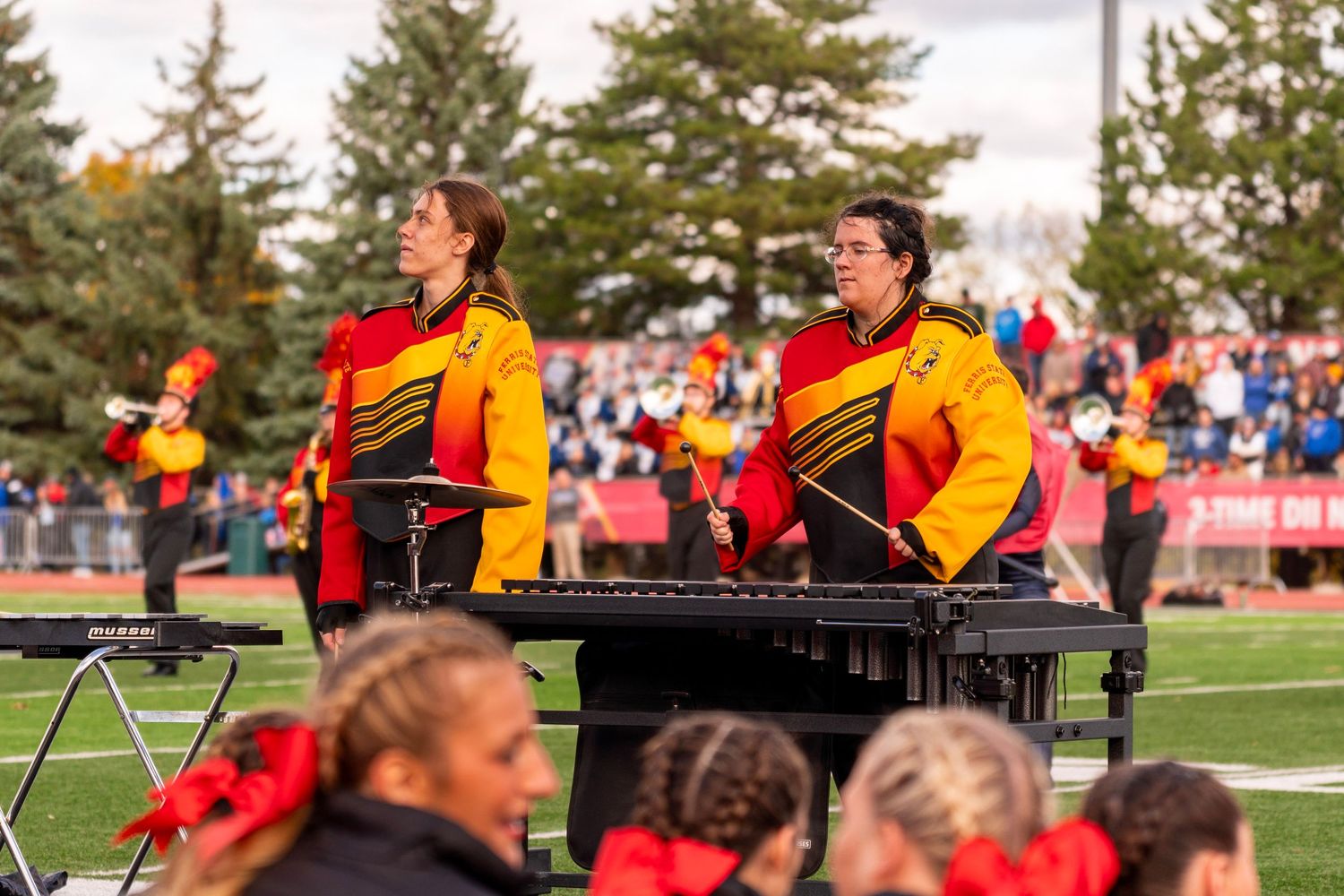 A marching band performs in formation on a football field wearing red and gold uniforms during a halftime show.
