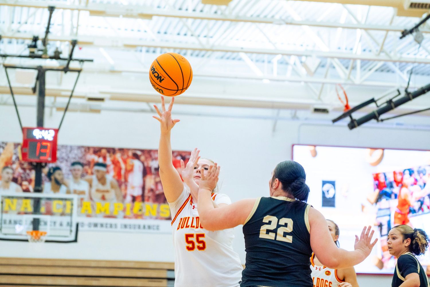 Basketball players compete for a rebound during an intense indoor game on a gymnasium court.
