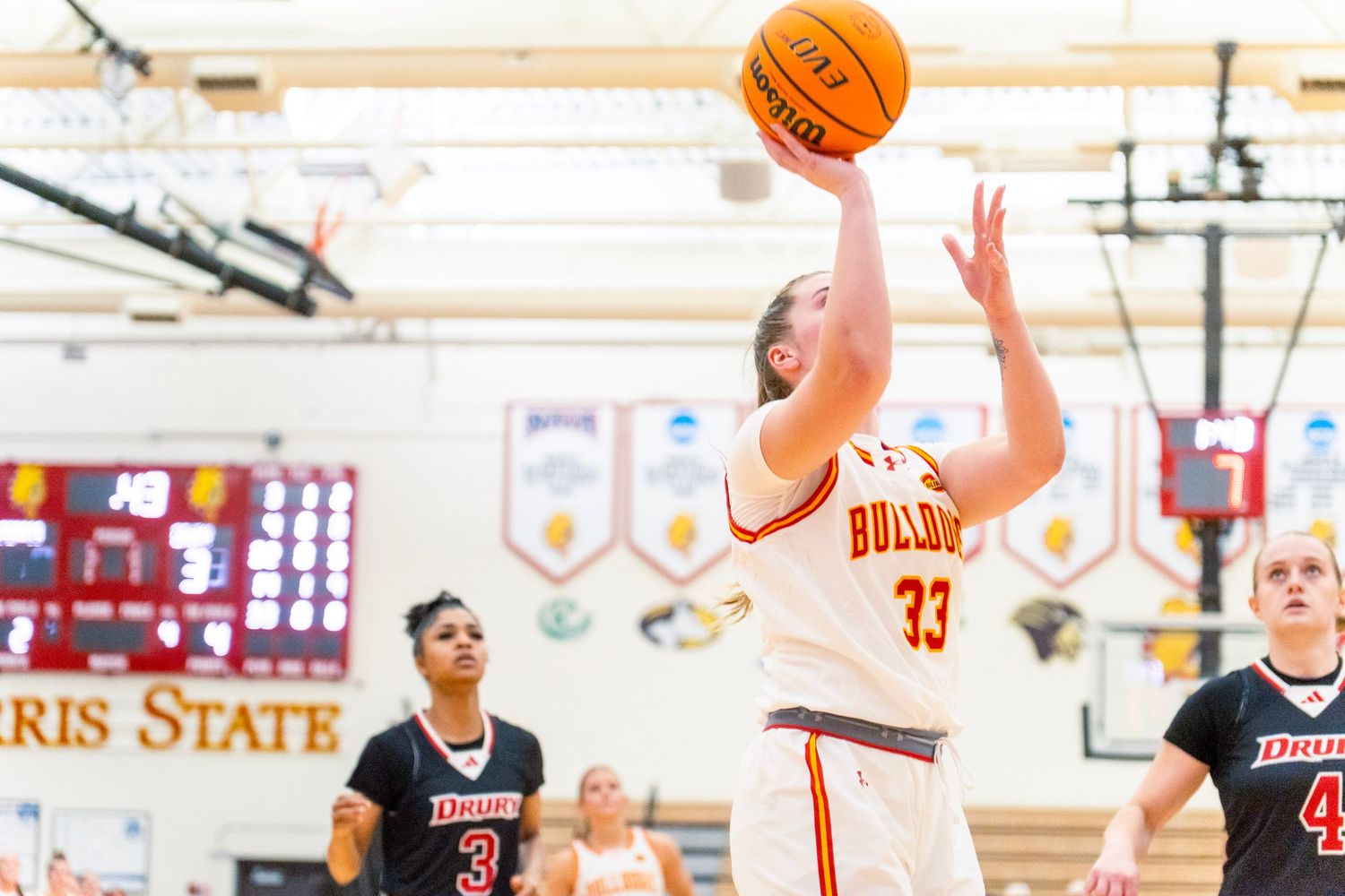 Basketball player takes a jump shot during a high school game with spectators watching in the gymnasium.
