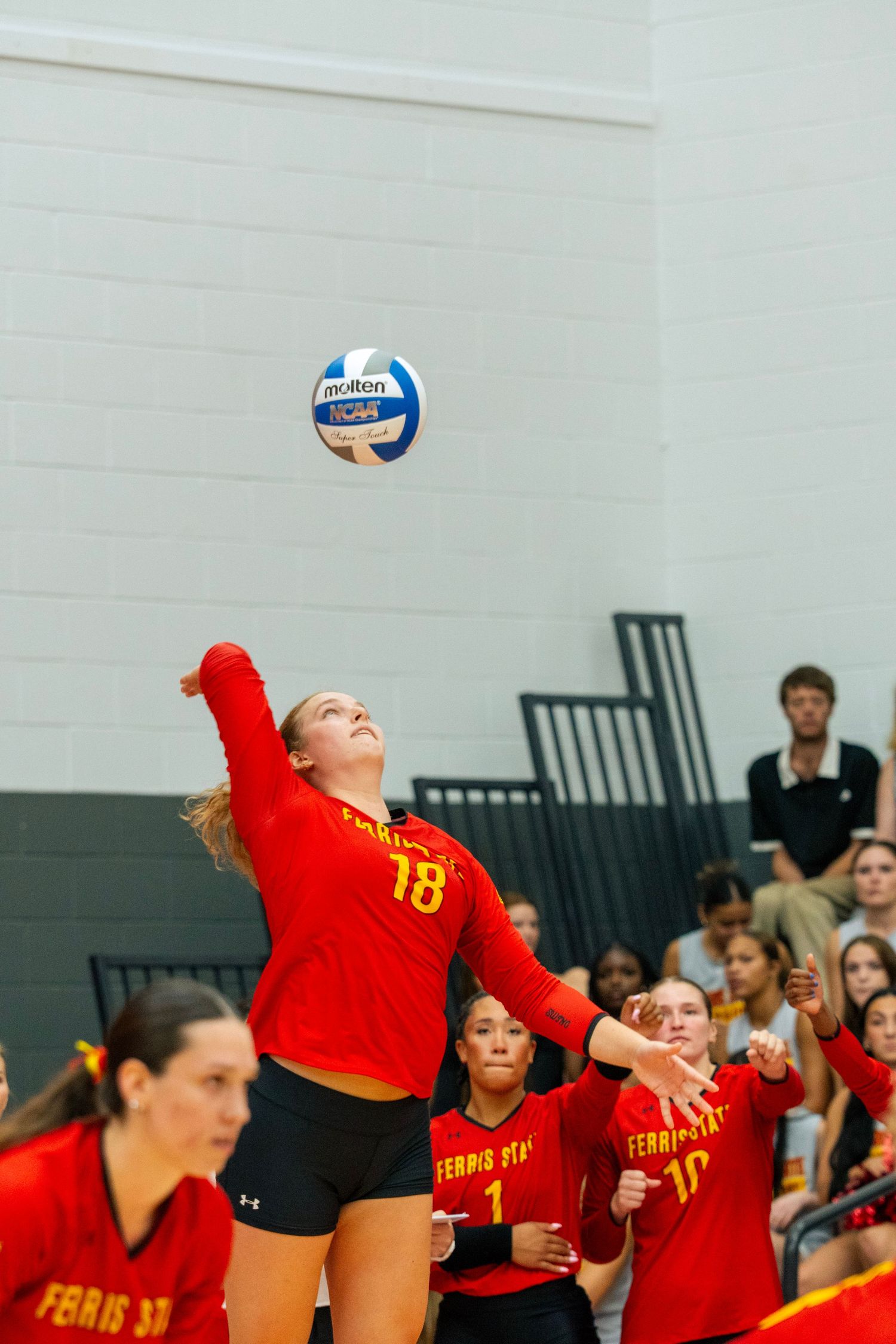 A volleyball player in a red jersey jumps high to spike the ball during a competitive game.