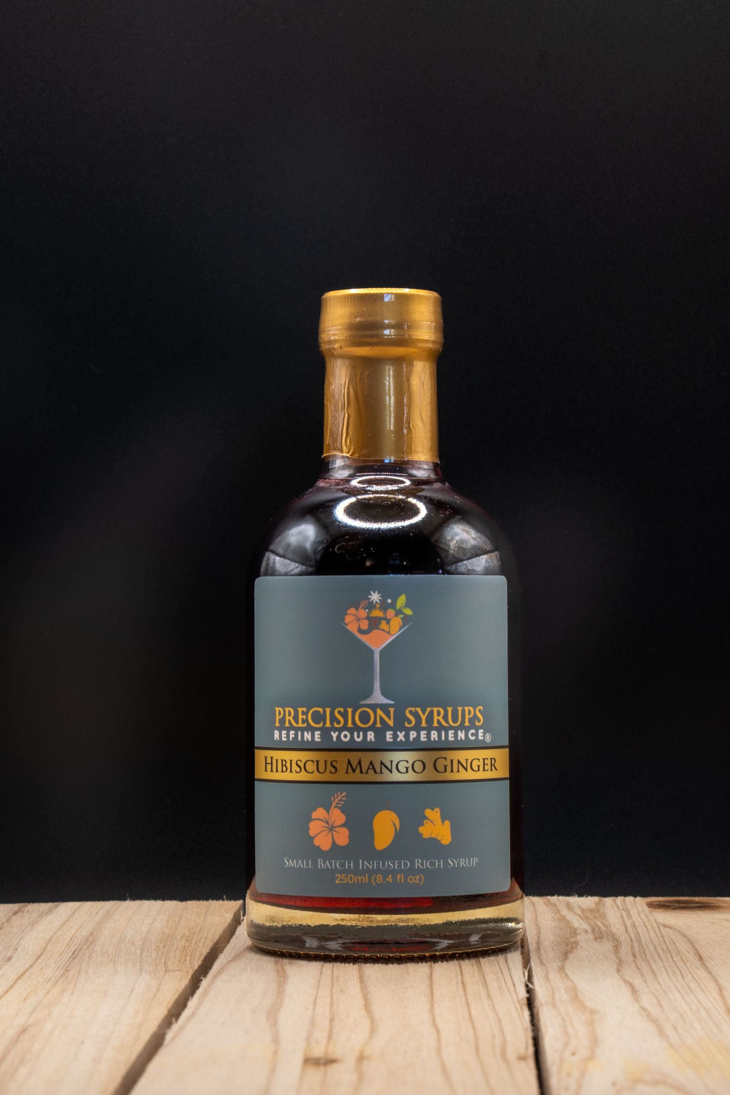 Glass bottle of Precision Syrups hibiscus mango ginger mixer on wooden table.