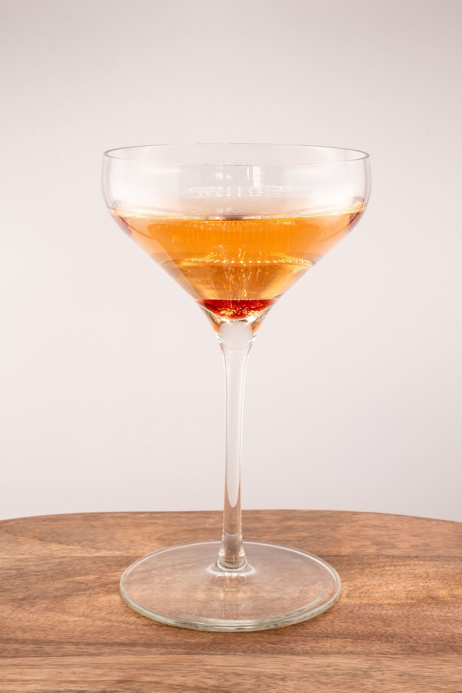 Golden-orange cocktail in a classic coupe glass displayed on rustic wooden surface against light background.