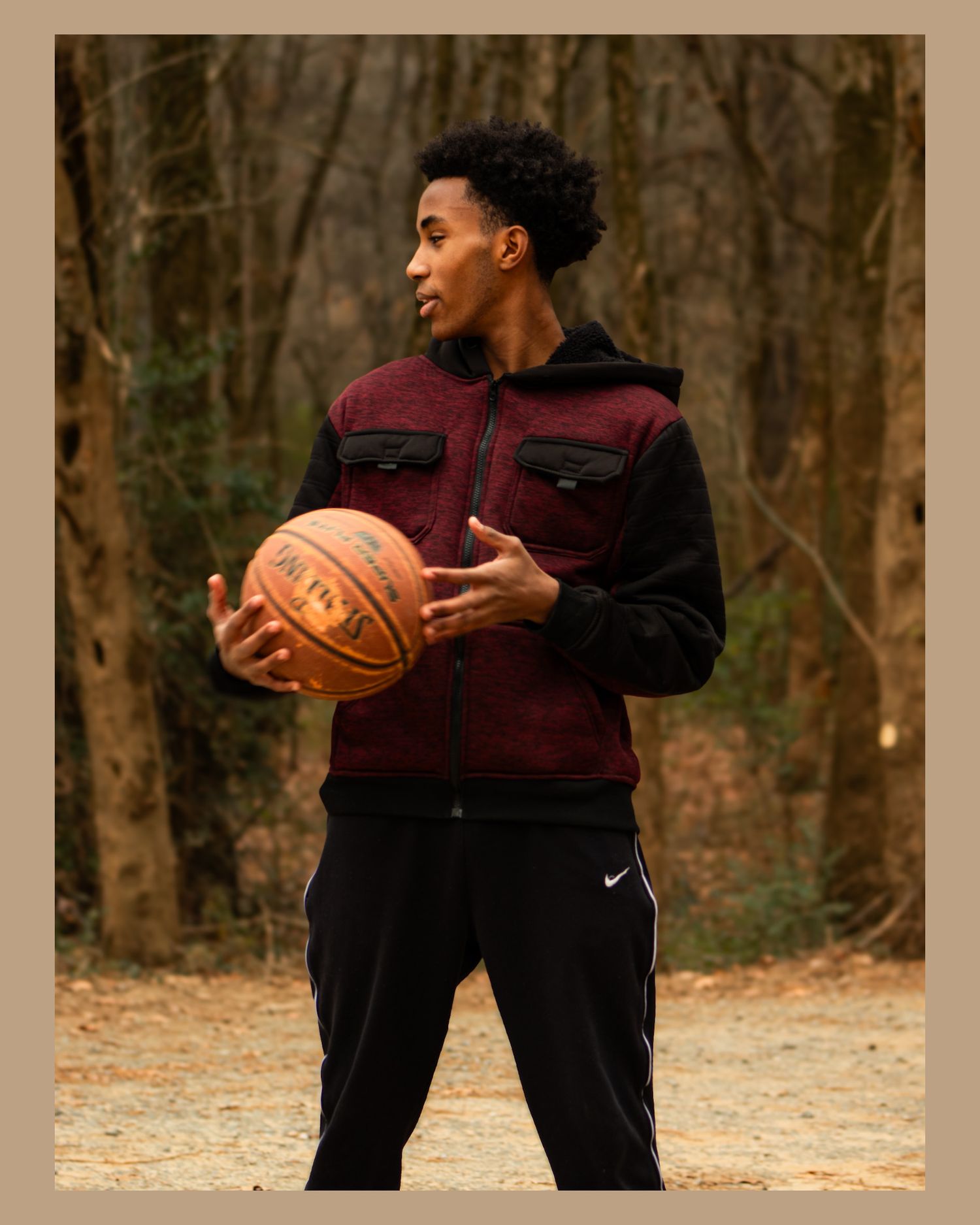 Person in burgundy jacket holding a basketball while standing in a wooded area.