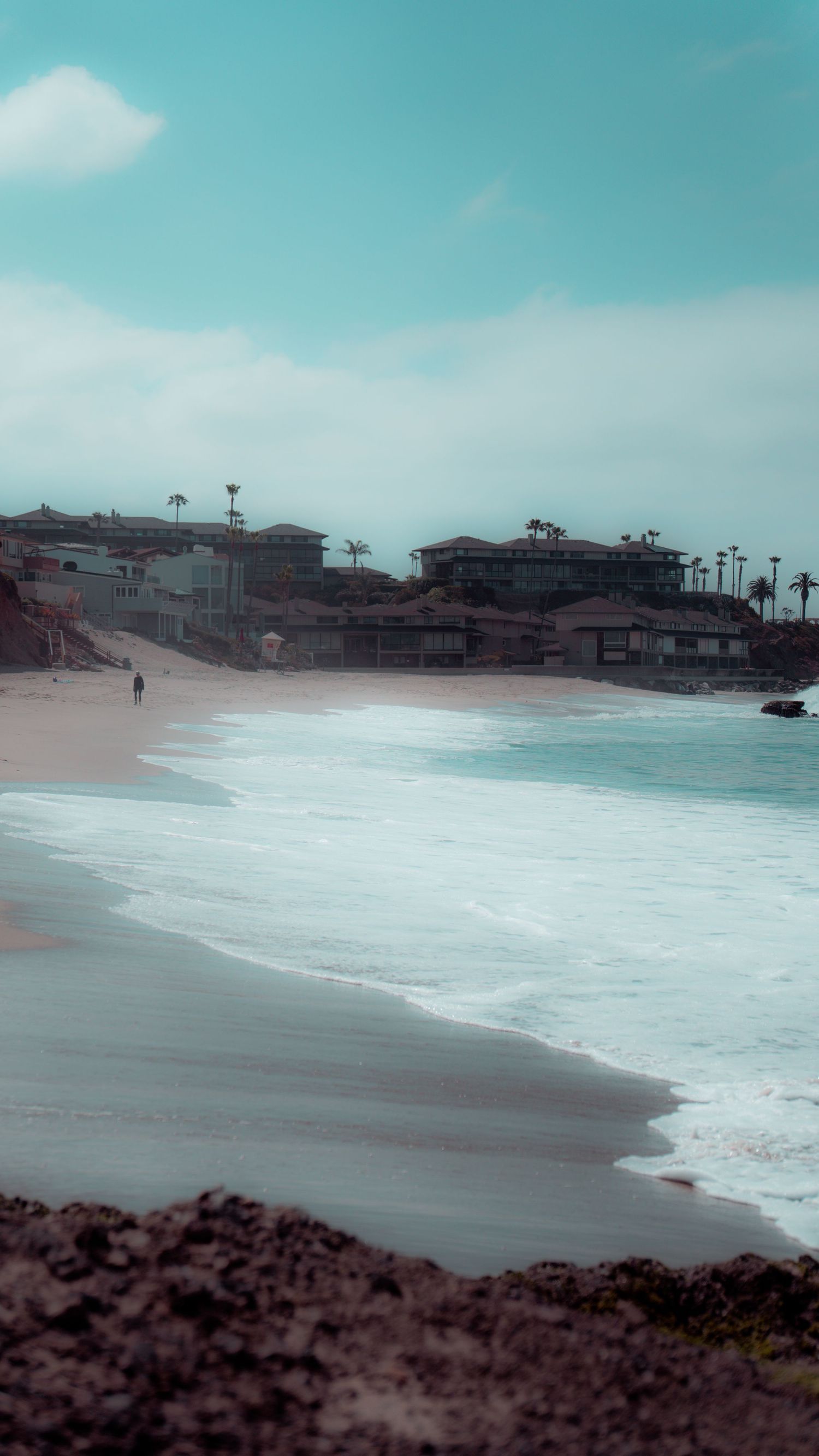 Moody beachfront with buildings and palm trees set against a misty turquoise ocean backdrop.