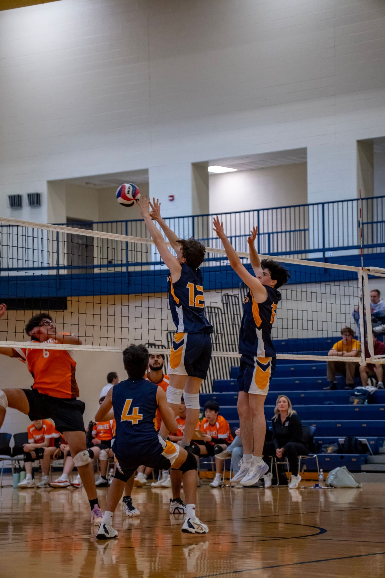 Players leap high to block and spike during a competitive volleyball match on an indoor court.