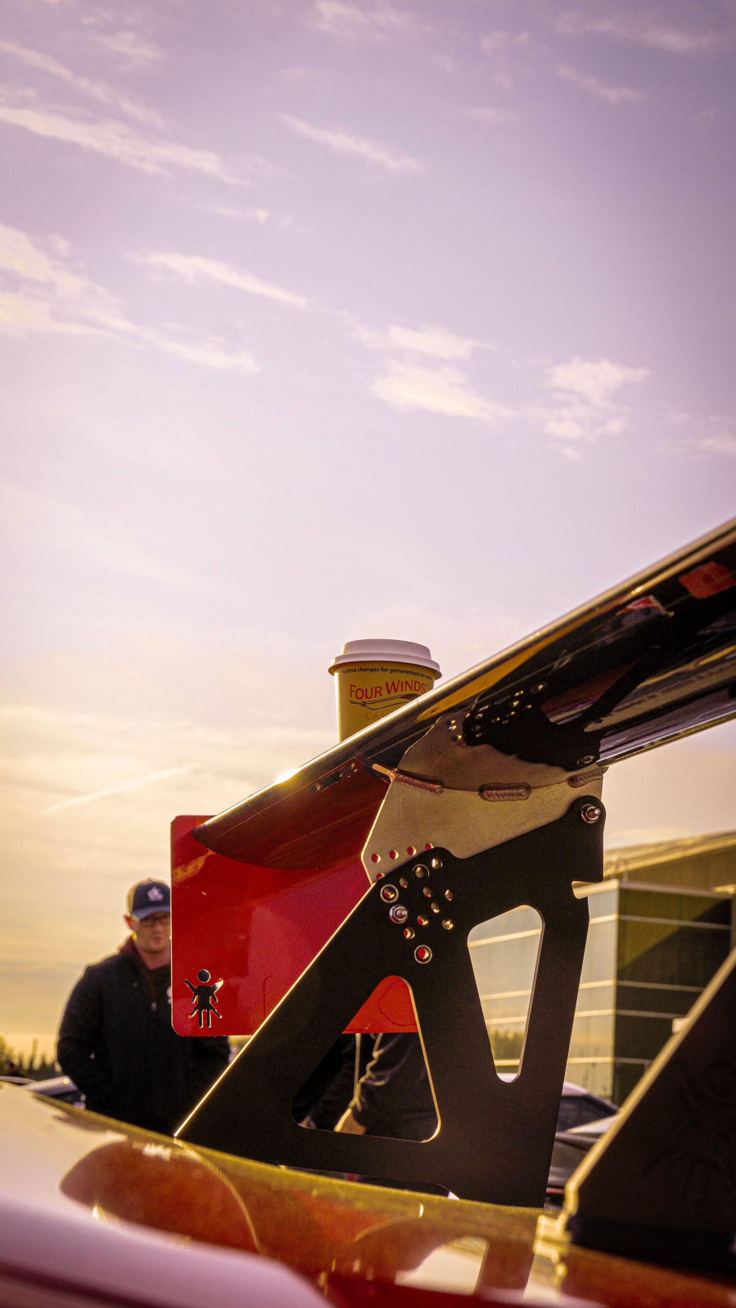 Rear wing and aerodynamic details of race car silhouetted against purple sunset sky.