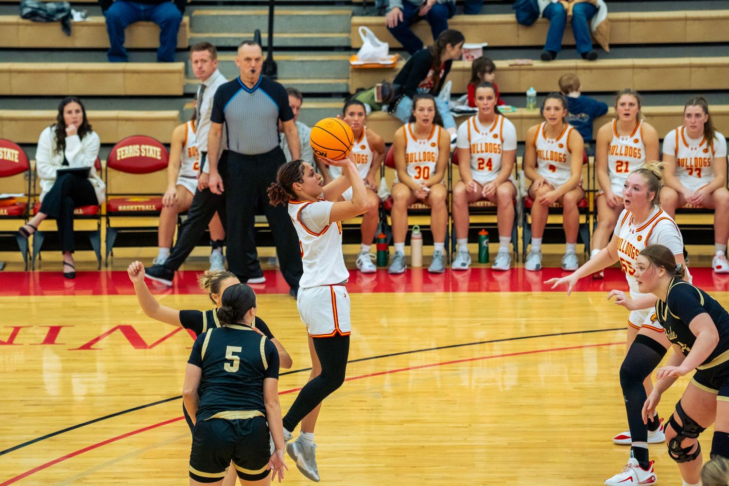 High school basketball players compete in an intense game on a wooden court with spectators watching from the sidelines.