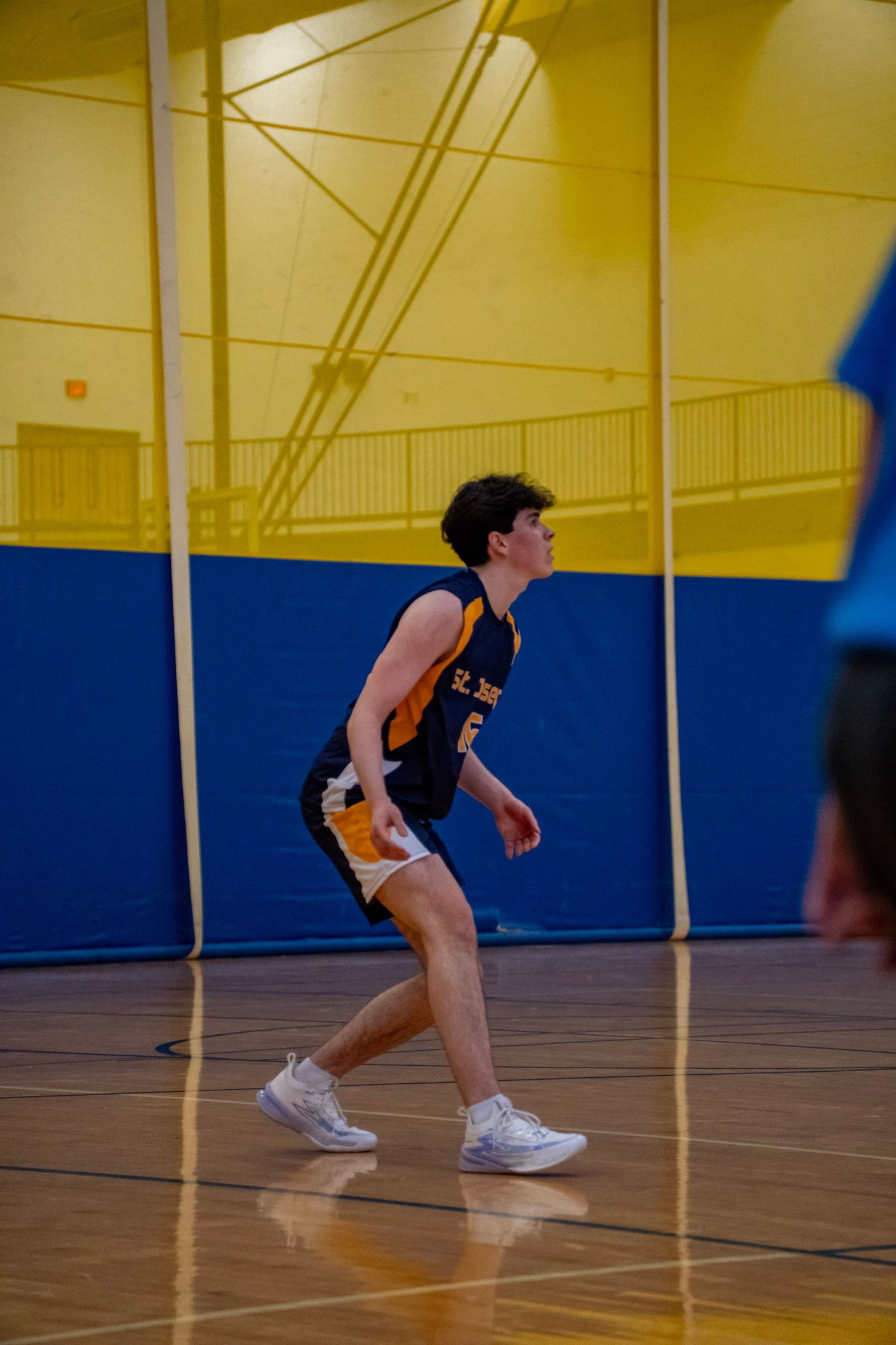 Player in navy uniform stretches low to dig an incoming volleyball on the hardwood court.