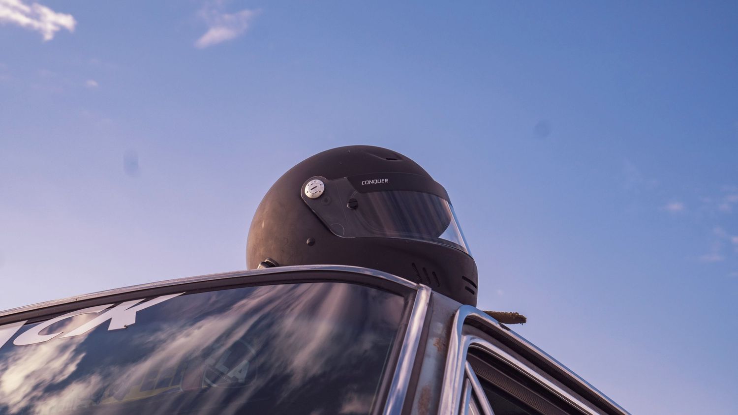 Racing helmet visible through car window against vibrant blue sky background.