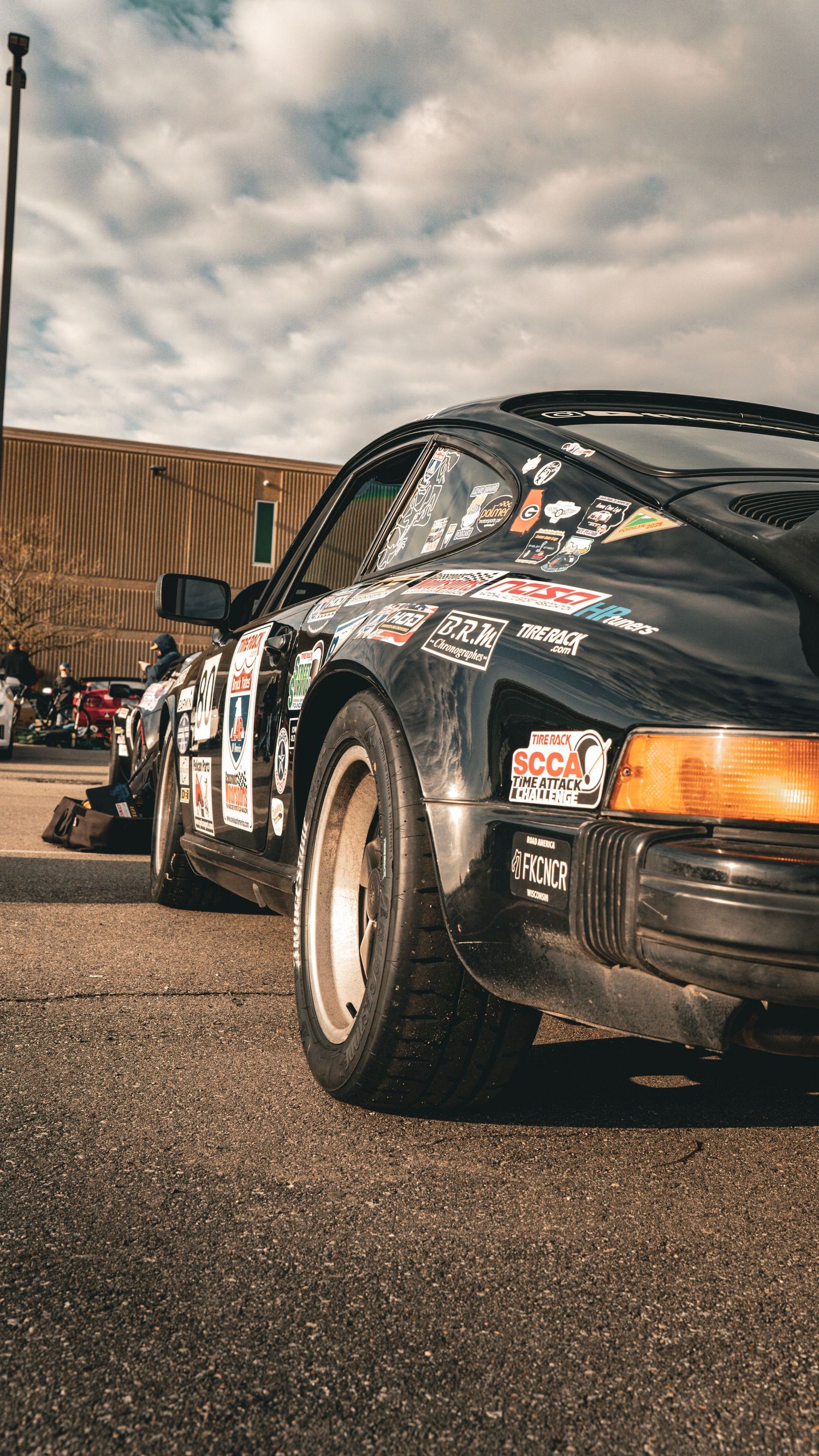 Side view of a modified Porsche 911 with wide body kit and racing decals parked in an outdoor setting.