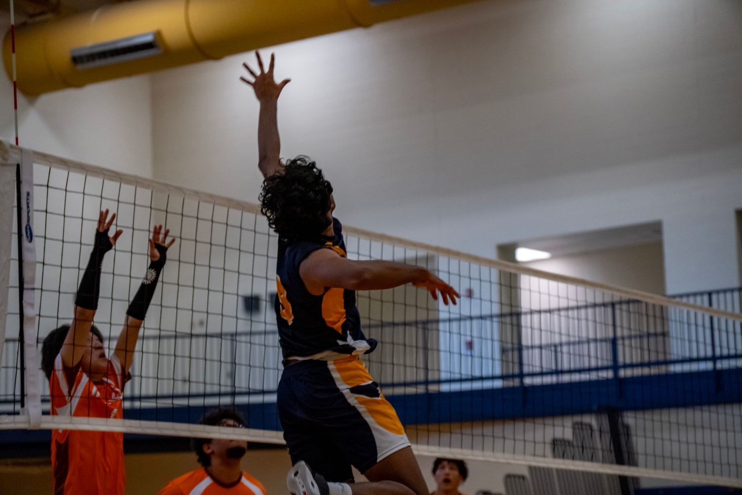 A volleyball player jumps to attack while opponents prepare to block at the net.