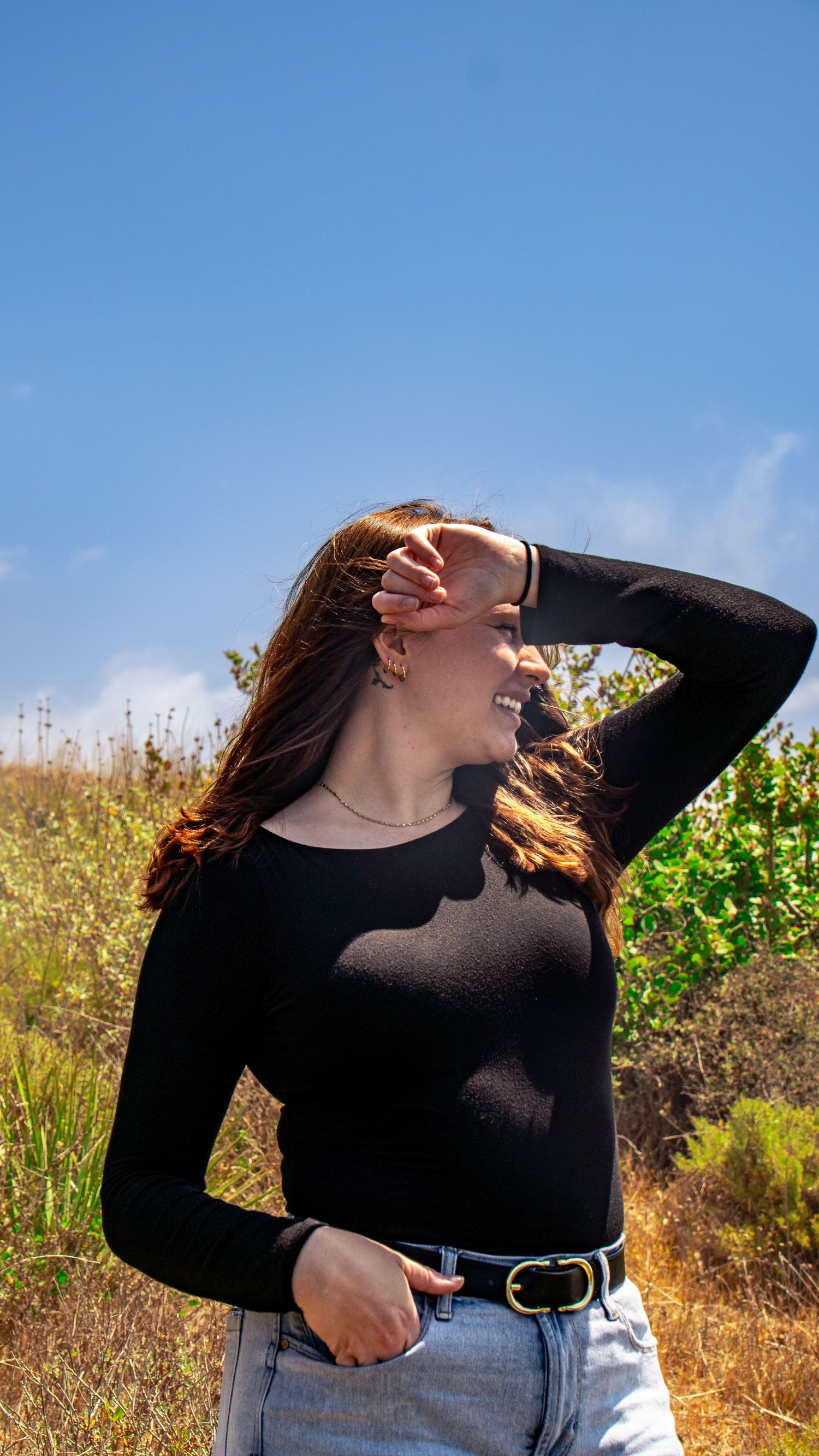 Person in black top laughing joyfully while posing against blue sky and golden grass.