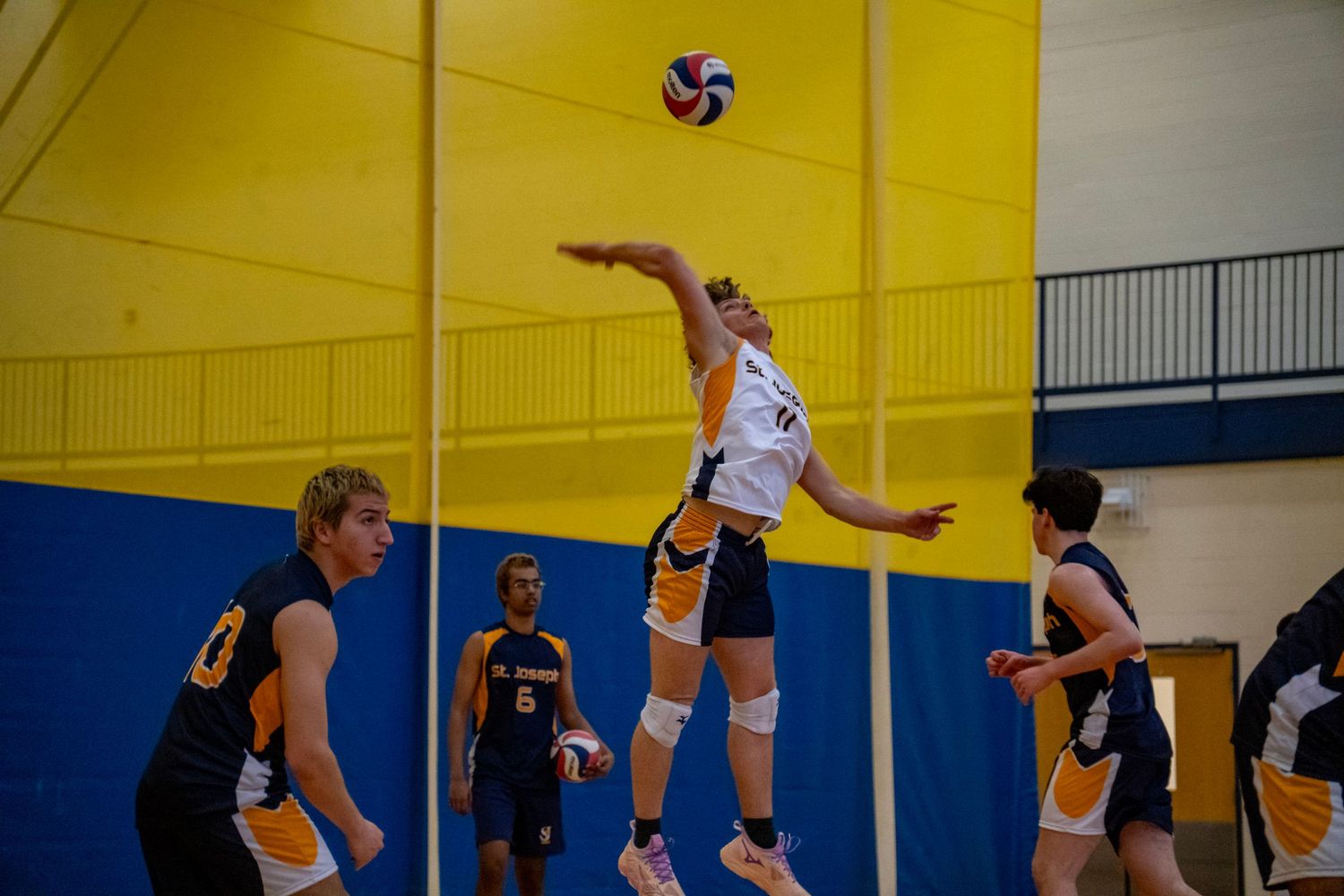 Player leaps for a powerful spike while opponents prepare to block during volleyball match.