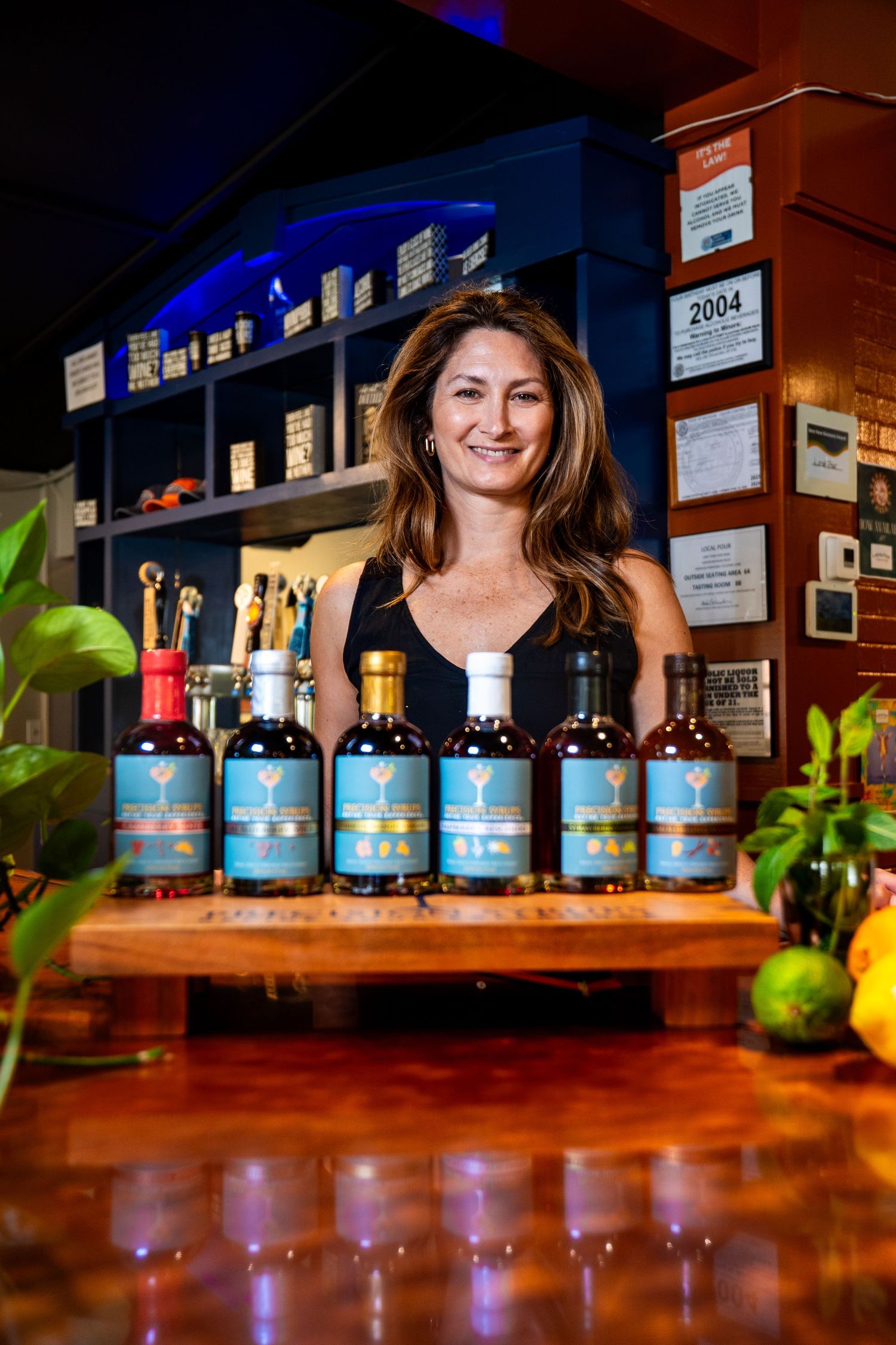 Premium spirits display on wooden bar counter with decorative plants and awards on wall.