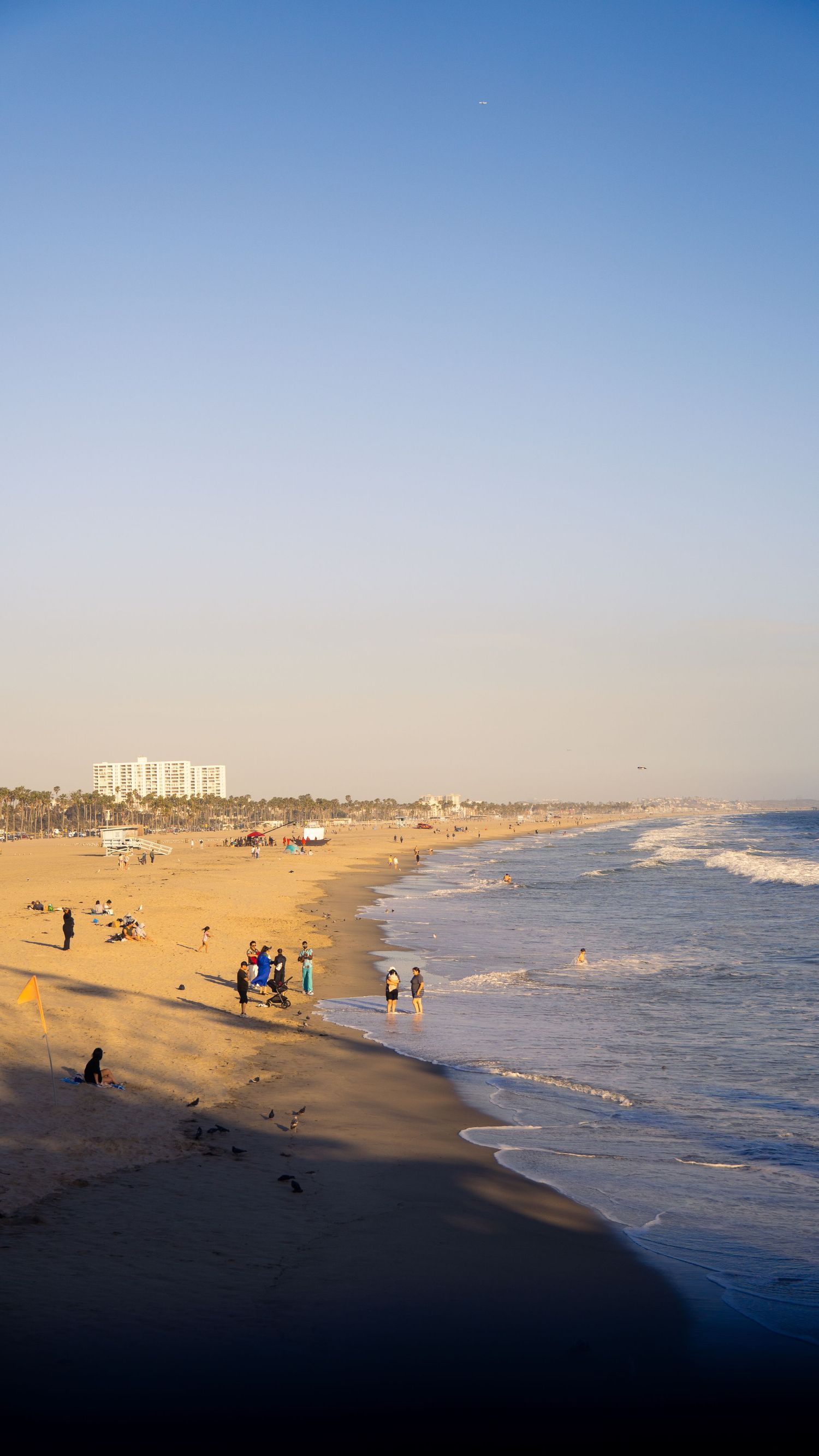 Golden afternoon light illuminates a beach scene with waves rolling onto shore.