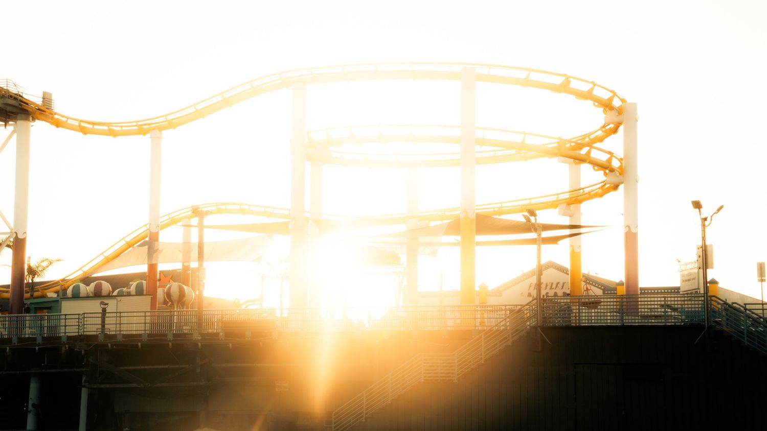 Roller coaster track silhouetted against bright sunburst at sunset at Pacific Park.