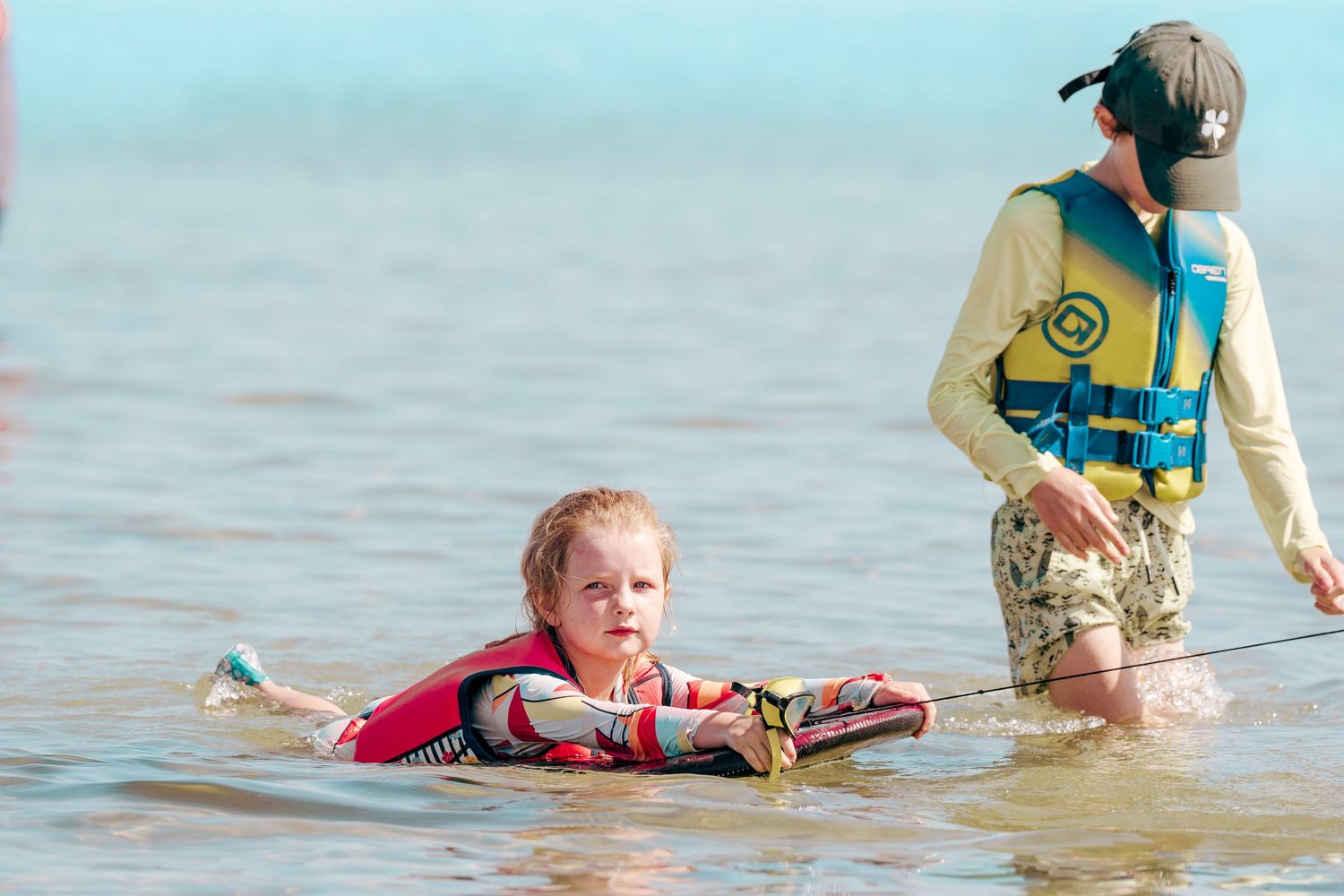 People wade and splash in shallow water together on a sunny summer day at a beach.