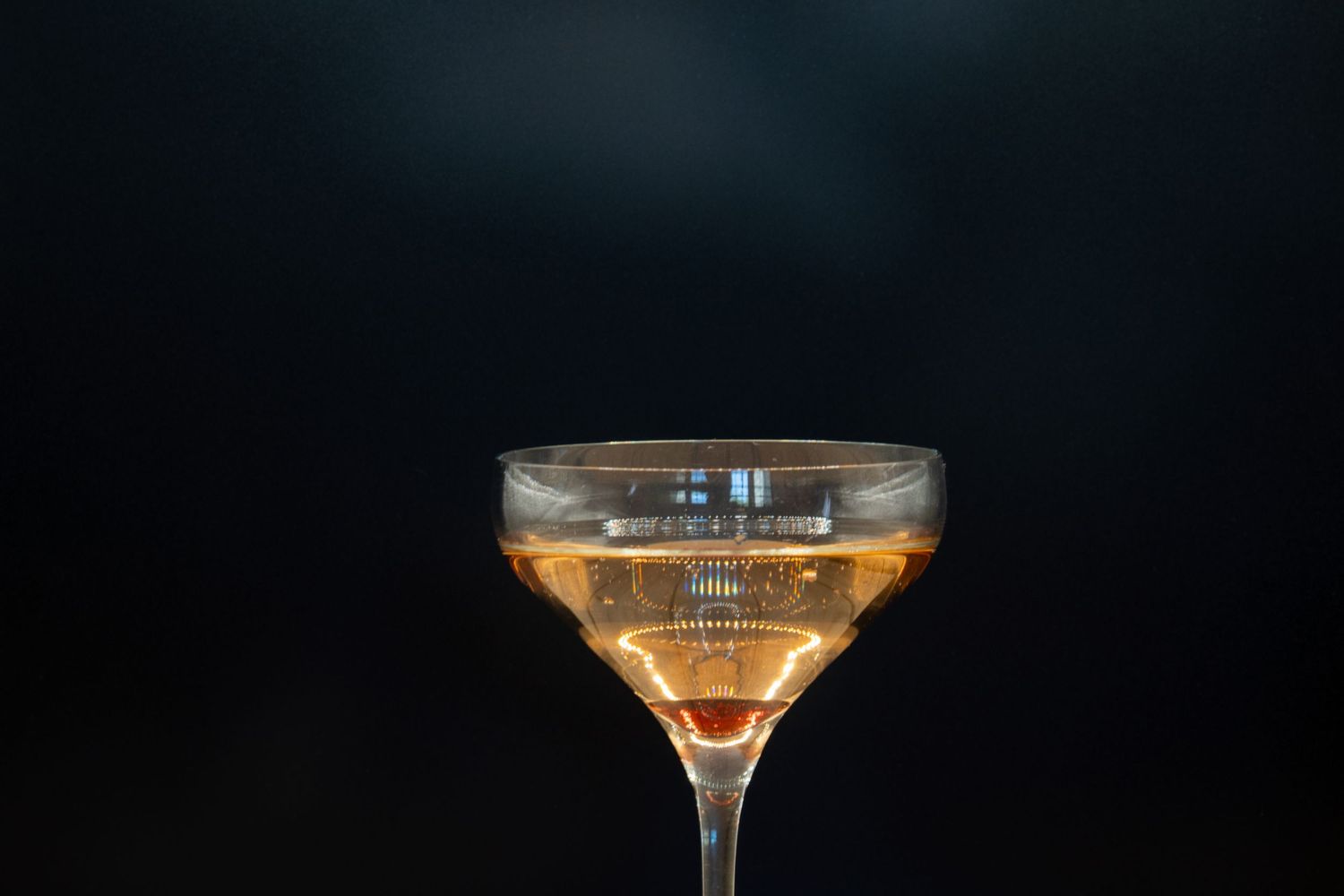 Crystal coupe glass filled with golden cocktail on rustic wooden surface against dark background.