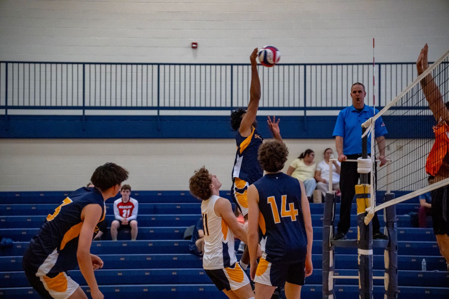 Volleyball players leap high to compete at the net during an intense match in a gymnasium.