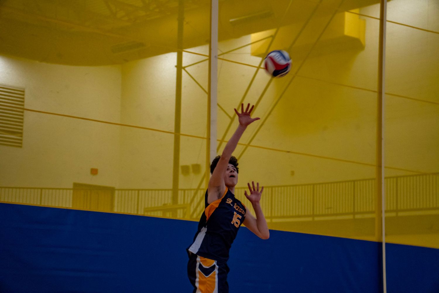 Athletic player in navy uniform jumps to spike volleyball during indoor match.