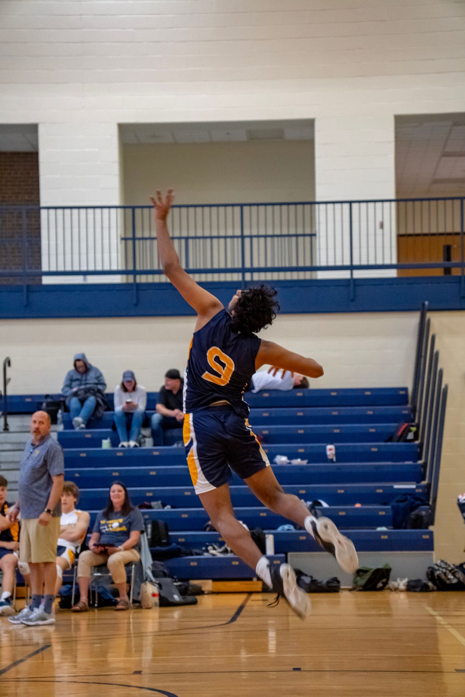 A player wearing jersey number 9 executes a powerful jump serve in an indoor volleyball game.
