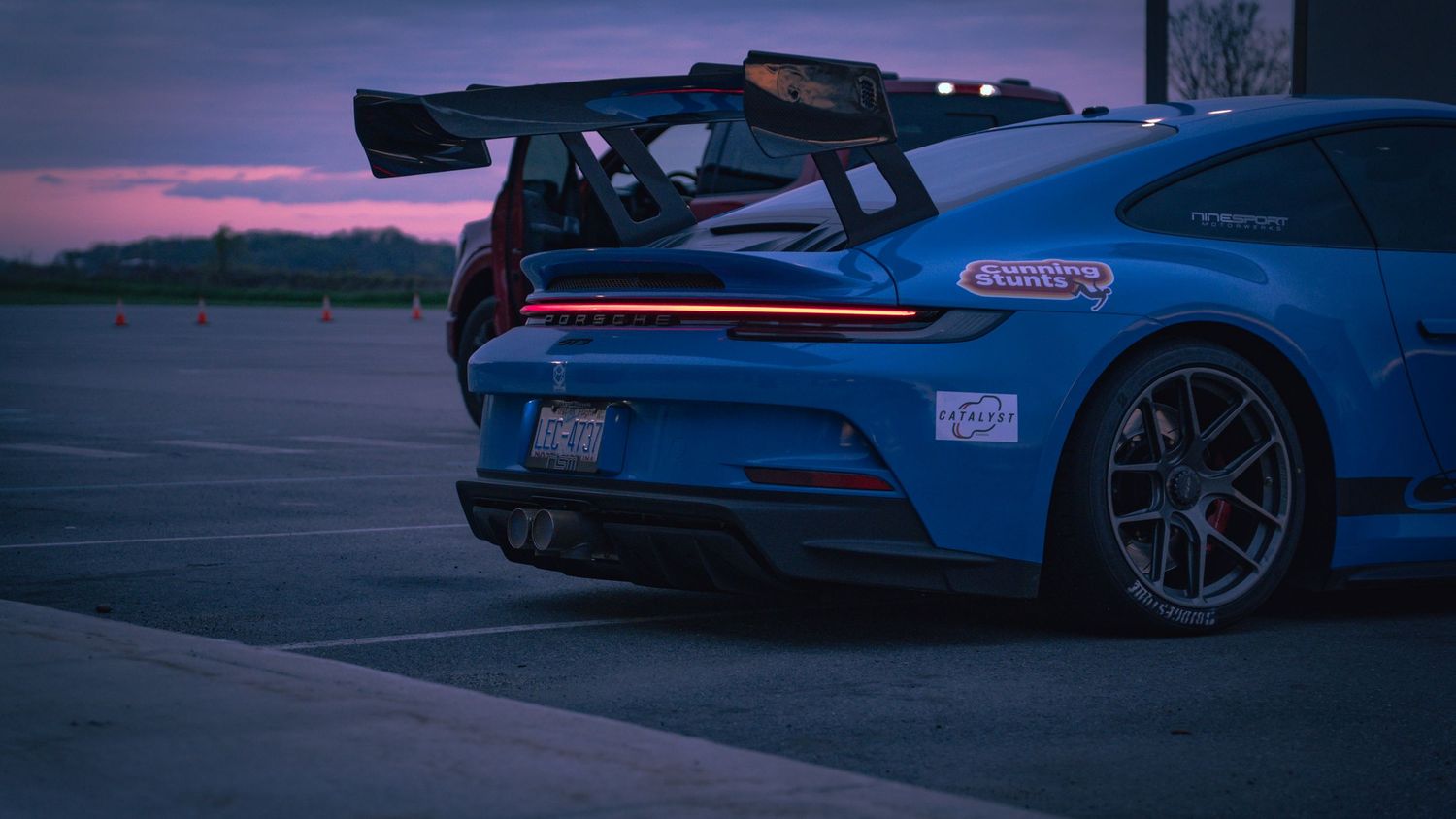 Rear quarter view of blue Porsche race car with GT wing at dusk.