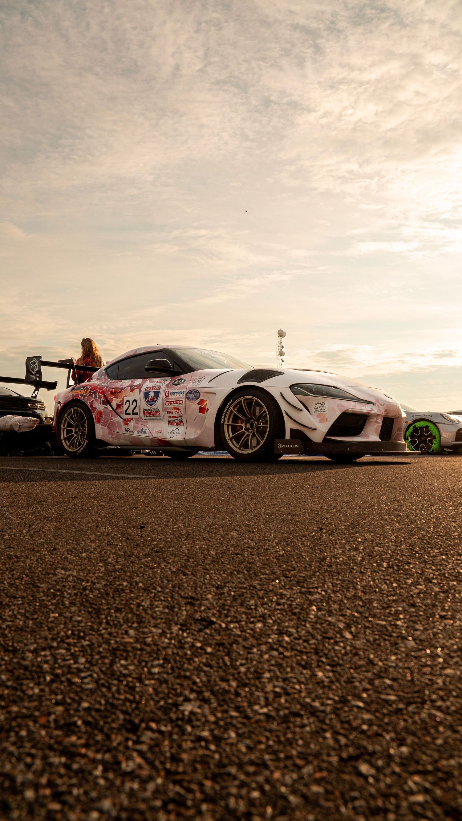 Low-angle shot of a modified white Toyota Supra with racing decals at dusk.